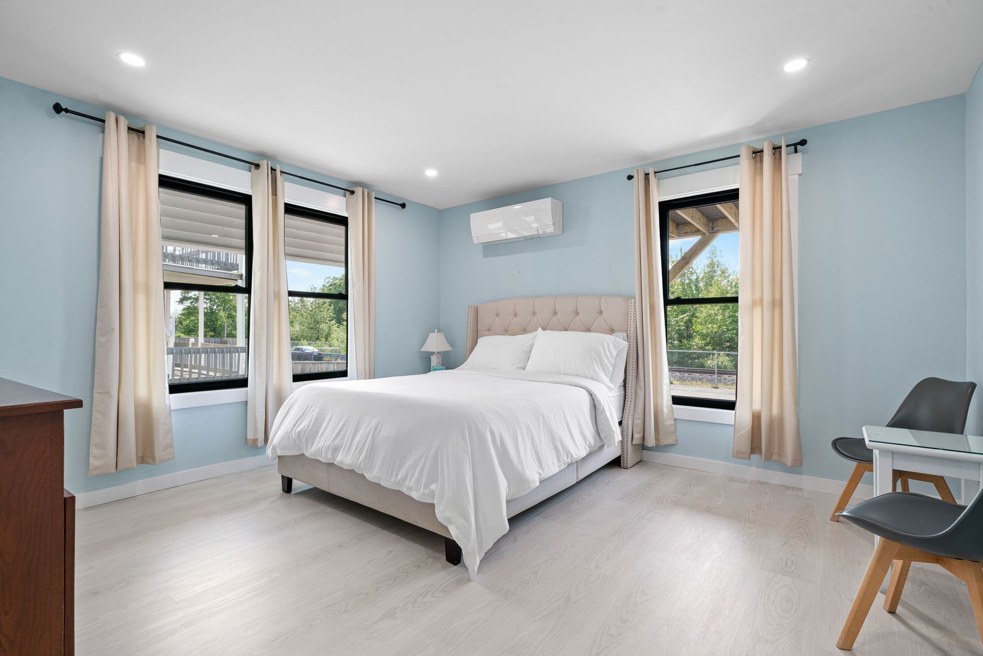 Bedroom with light blue walls, white bed, and natural light from windows.