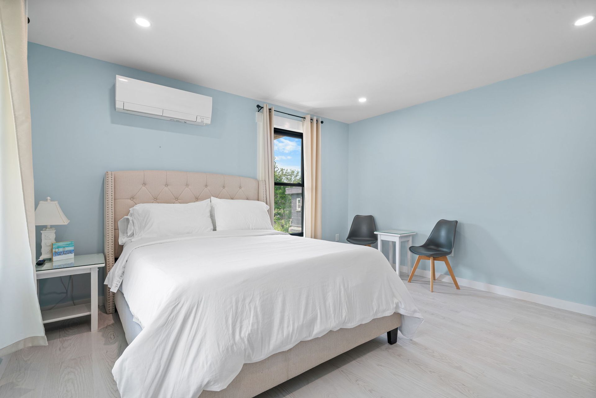 Bedroom with light blue walls, a bed with white linens, two chairs, and a small table.