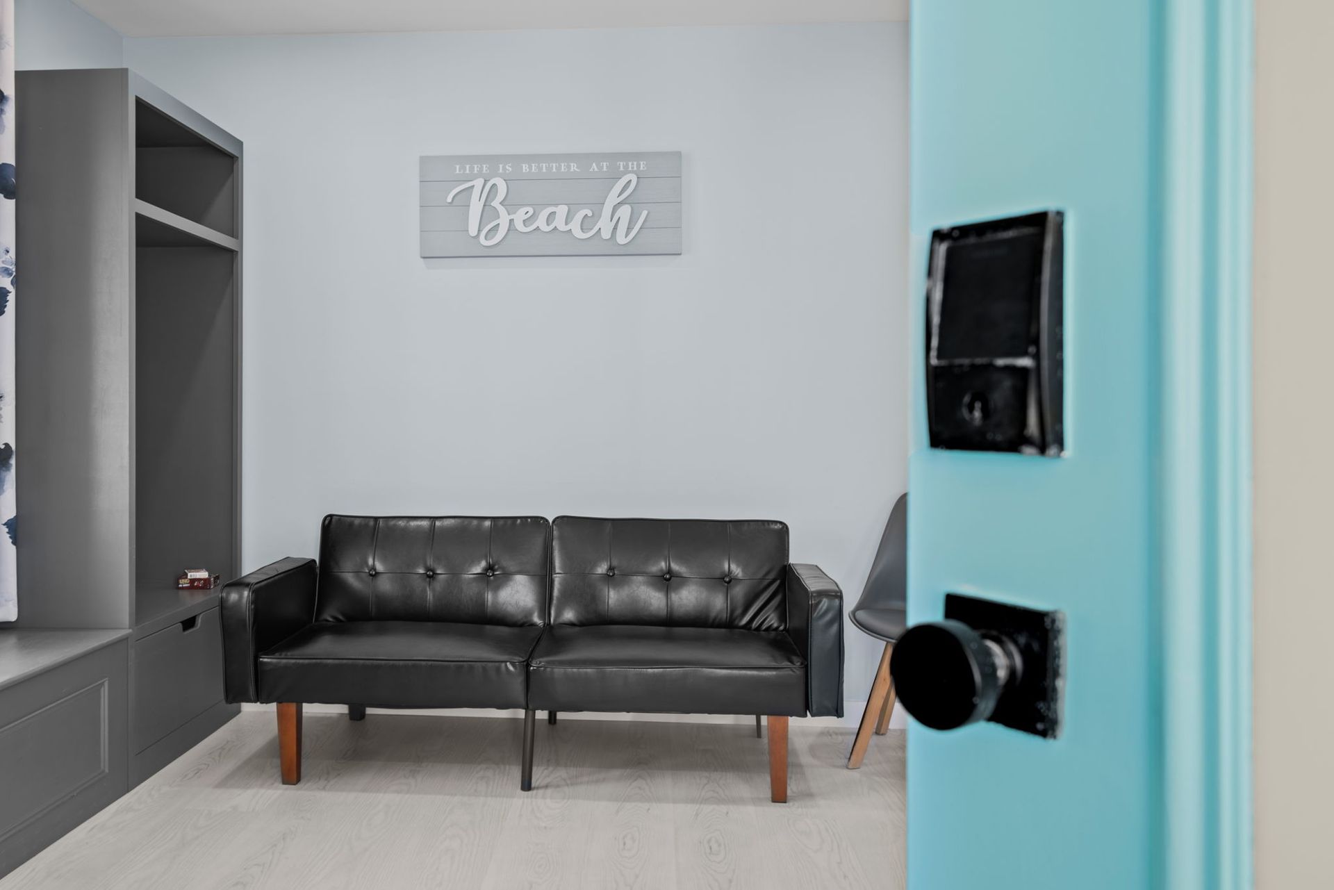 A waiting area with a black couch, grey walls, and a blue door with a black door handle.