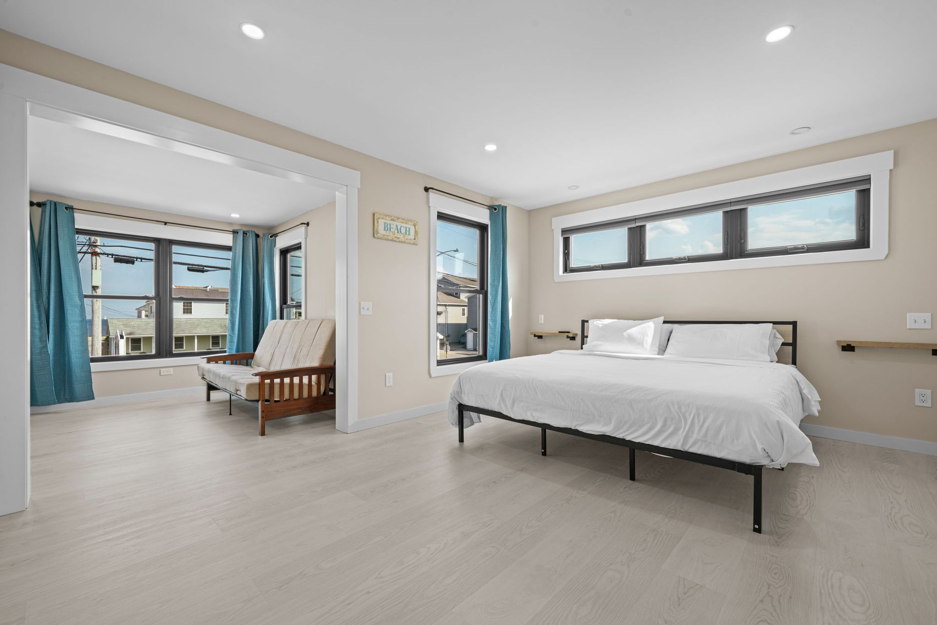 Spacious bedroom with a bed and a futon, light wood floors, and large windows.