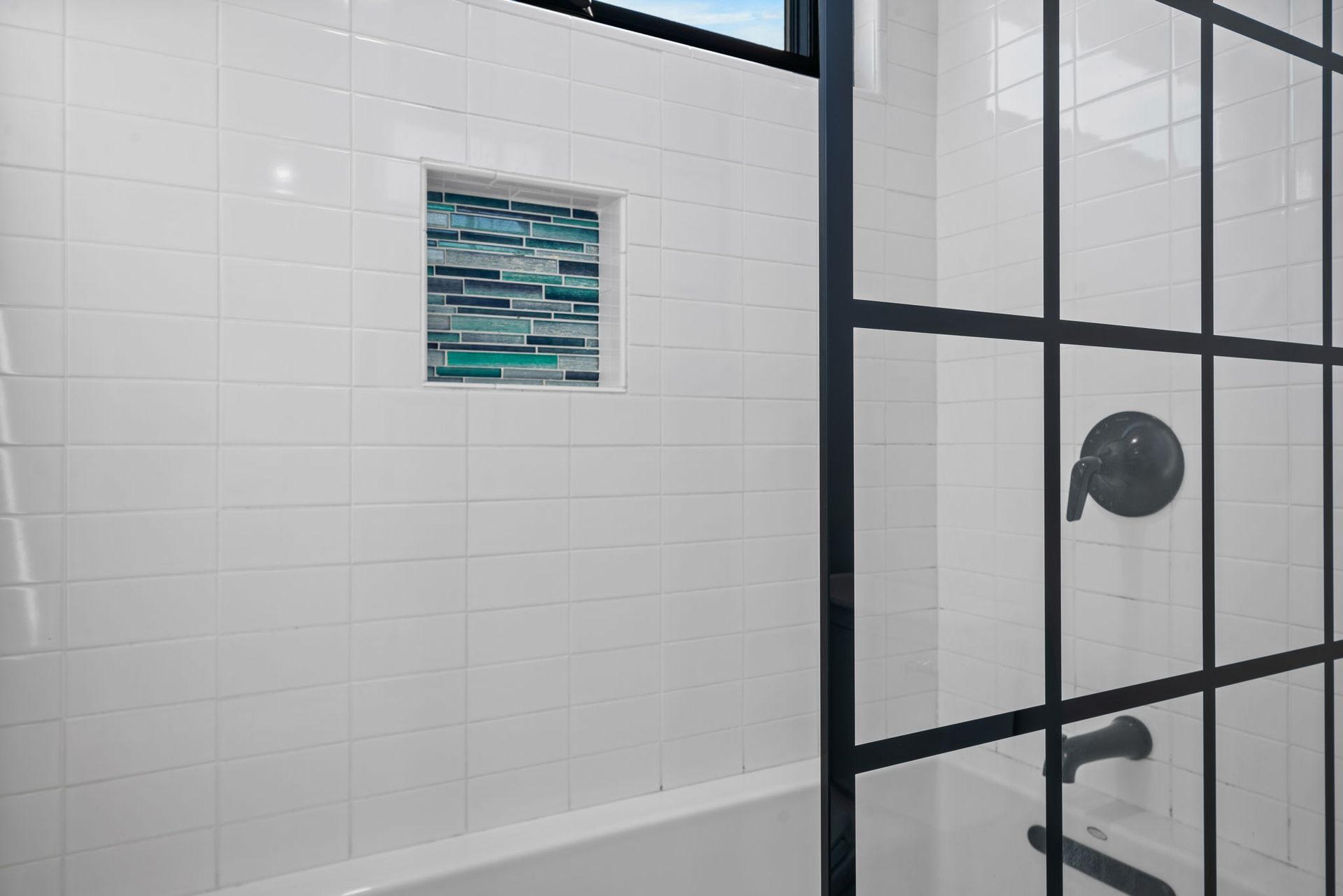 White tiled bathroom with black framed shower door, a decorative tile niche.
