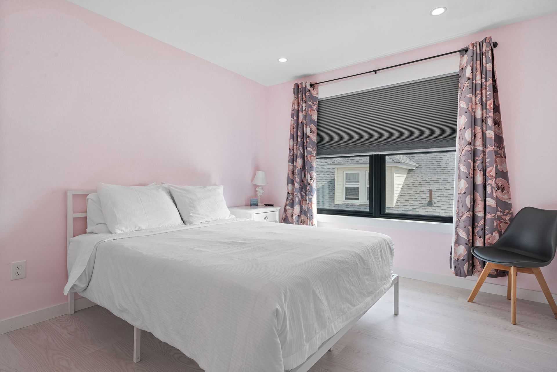 Pink bedroom with white bed, floral curtains, and gray chair.