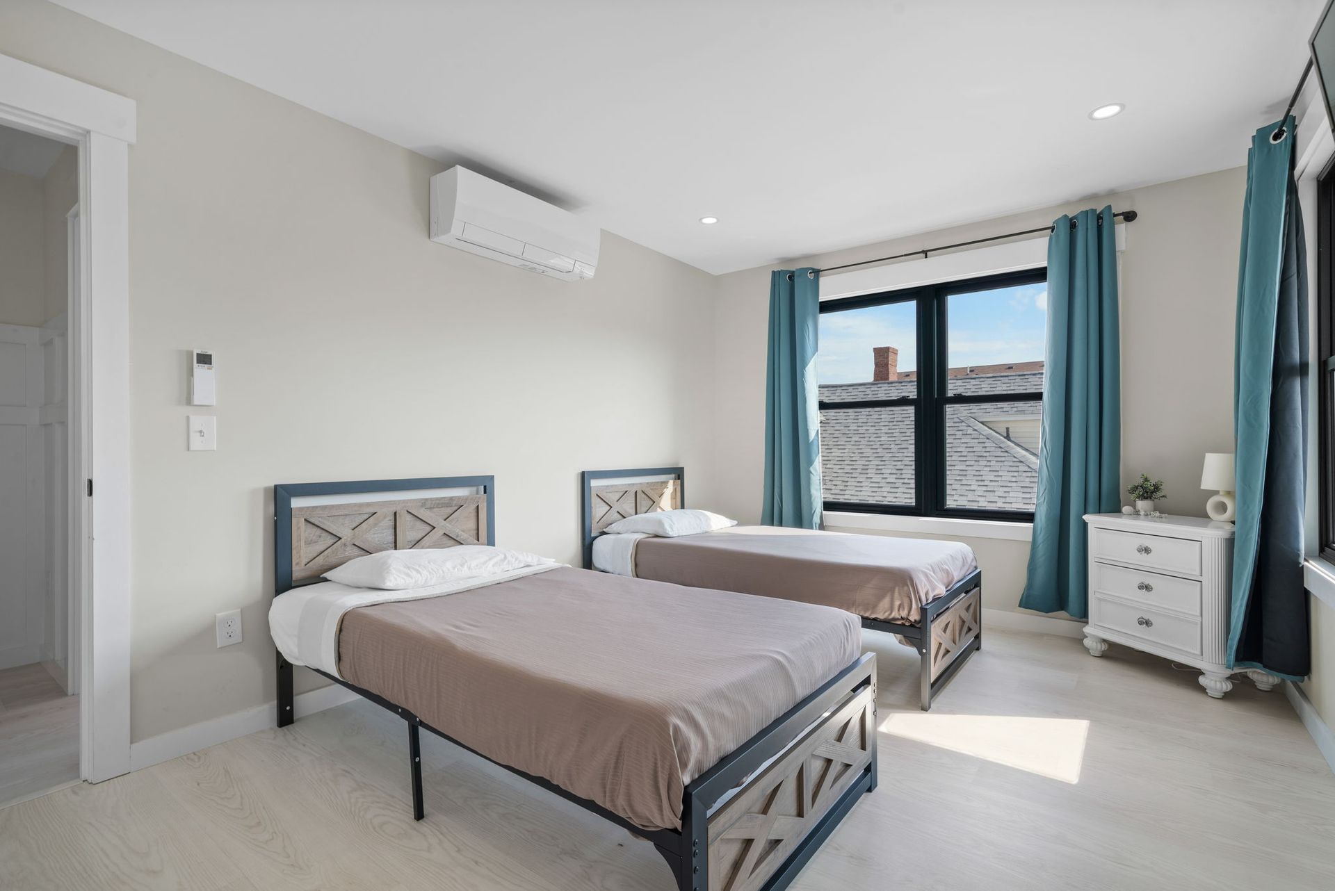 Two twin beds in a bedroom with a window and turquoise curtains.
