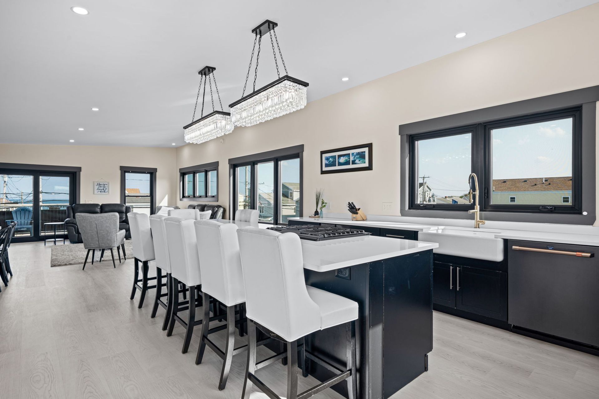 Modern kitchen with island, white chairs, dark cabinetry, large windows, and light wood floors.