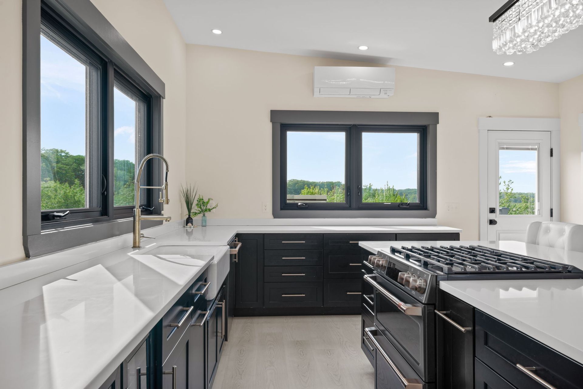 Modern kitchen with dark cabinets, white countertops, large windows, and a gas stove.