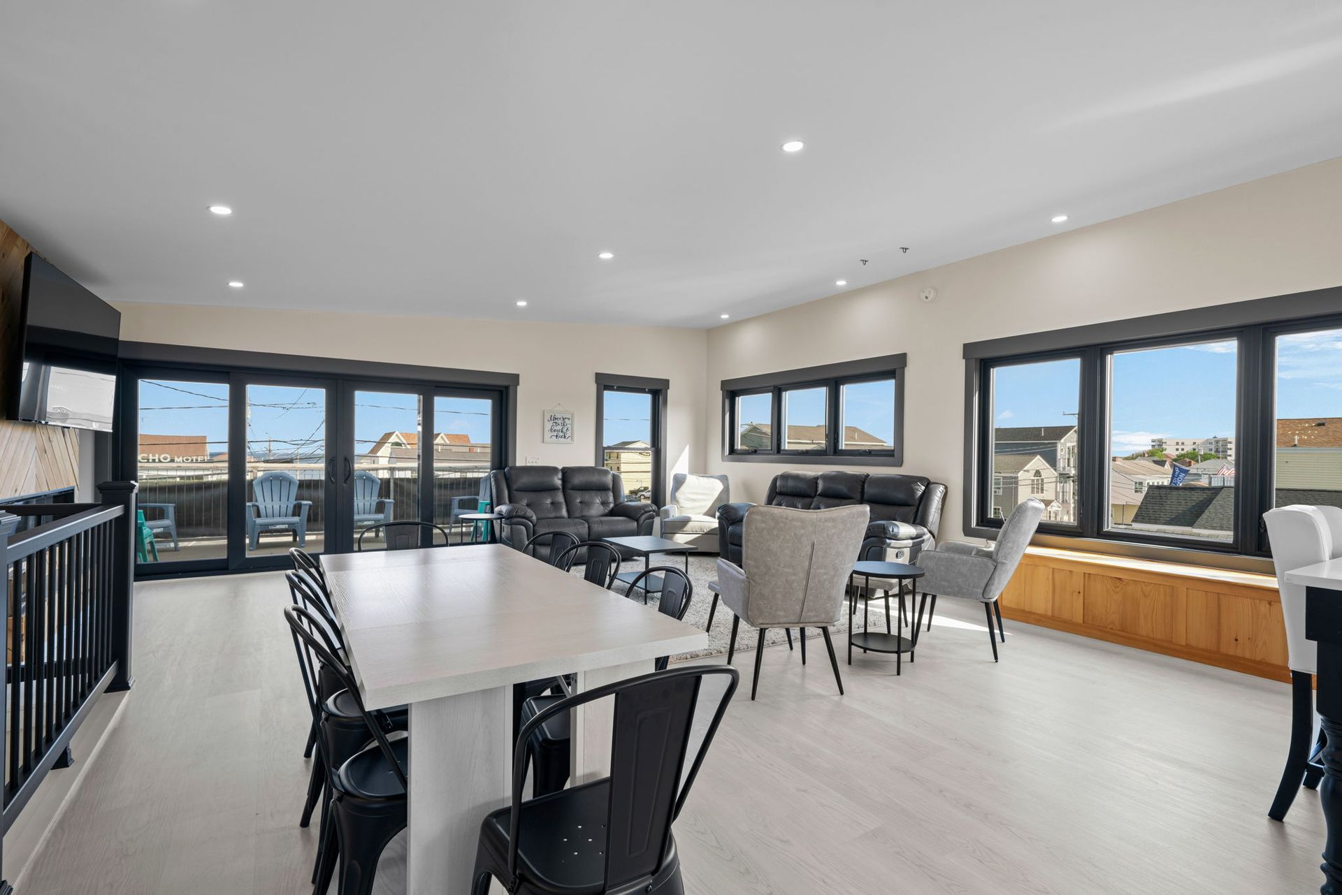 Open-concept living space with large windows, a dining table, seating area, and access to a deck.