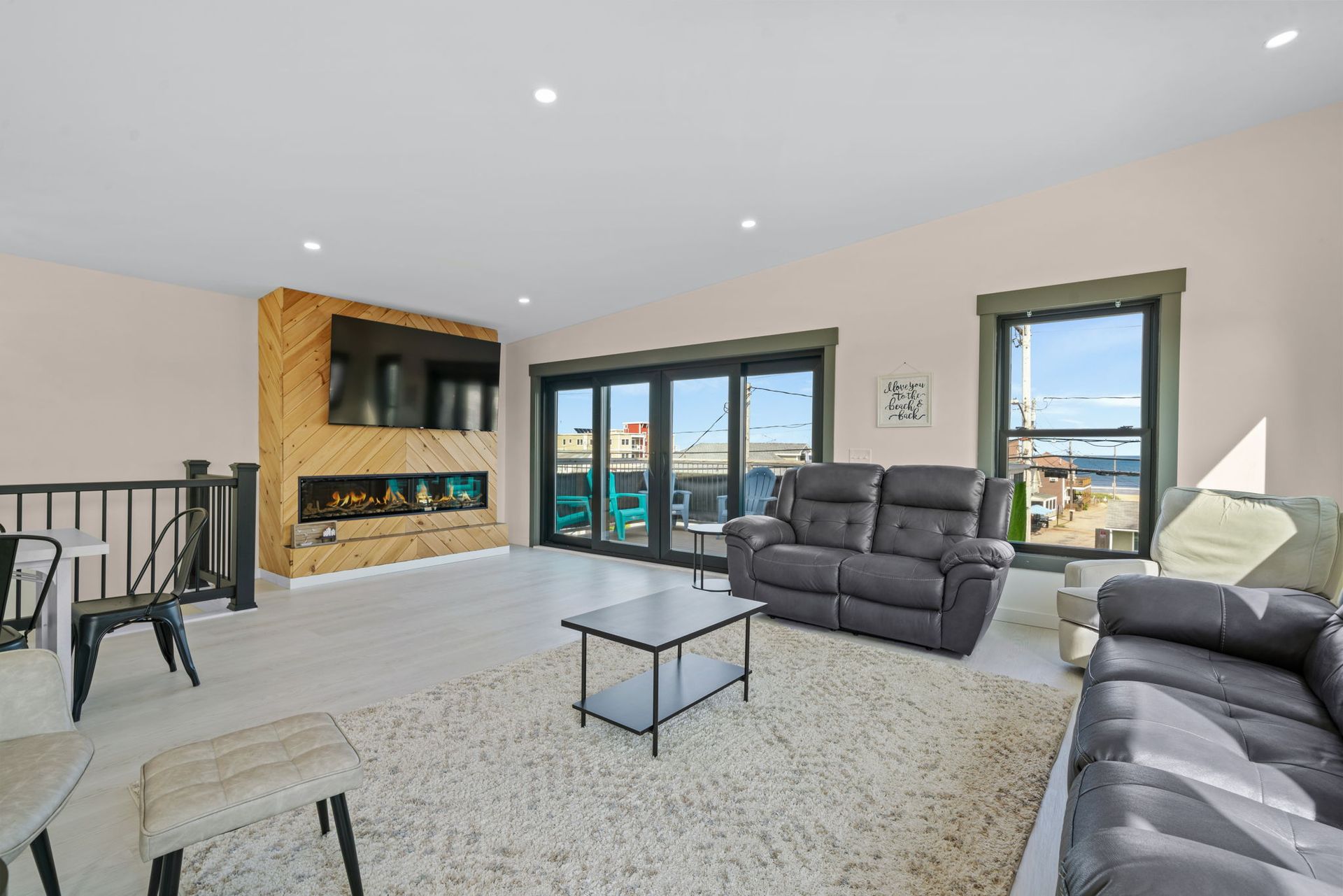 Living room with fireplace, TV, gray couches, white rug, and sliding glass doors.