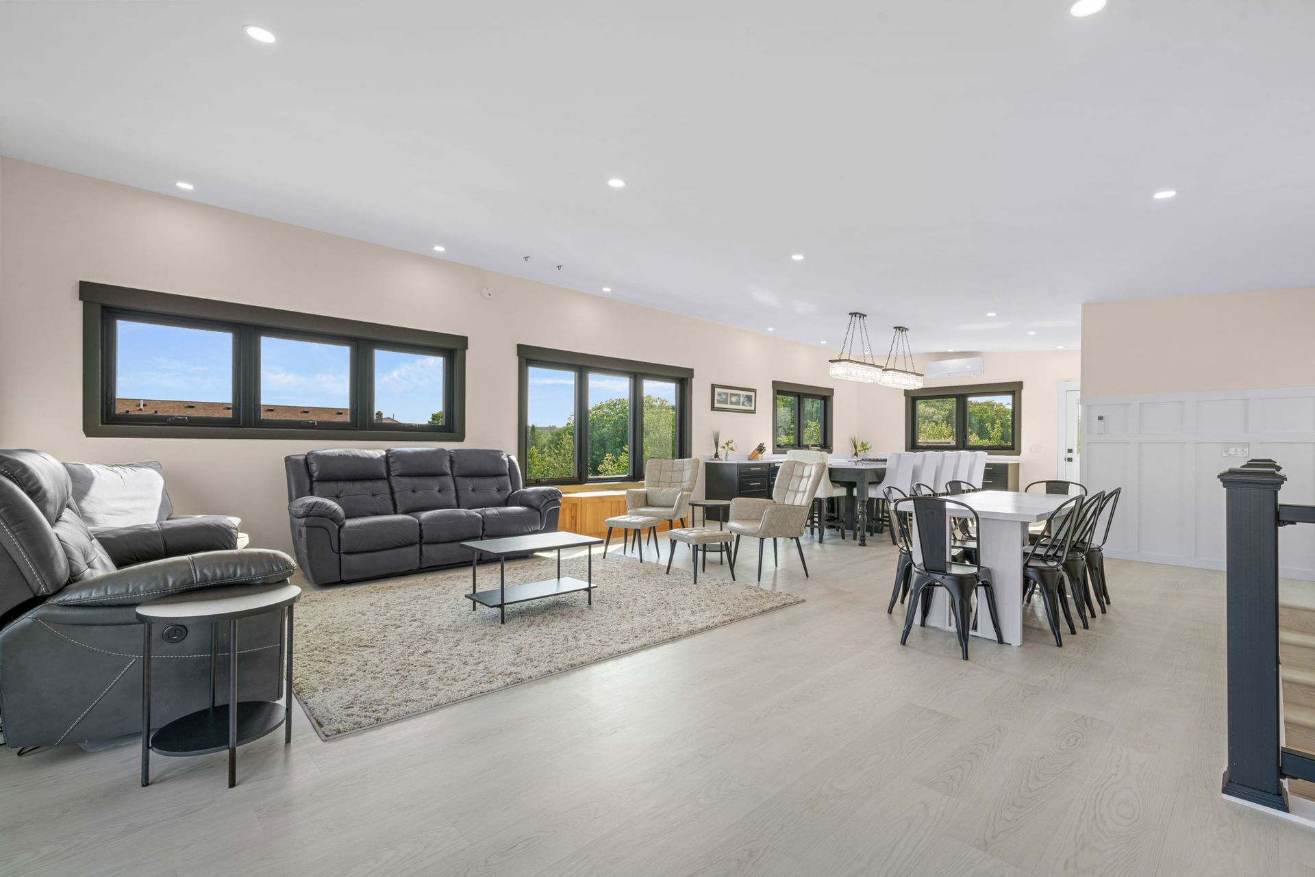 Spacious open-plan living area with a sofa, dining table, windows, and hardwood floors. Neutral tones and natural light.