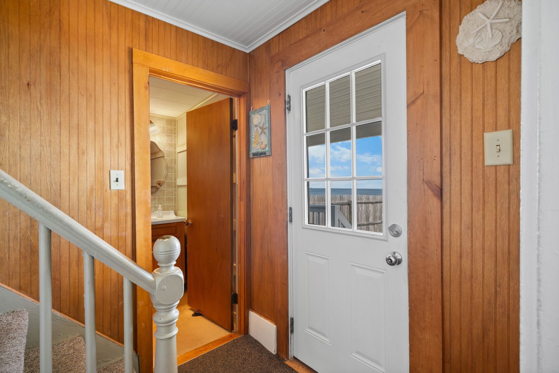 Hallway with wooden walls, open bathroom door, and white door with ocean view.