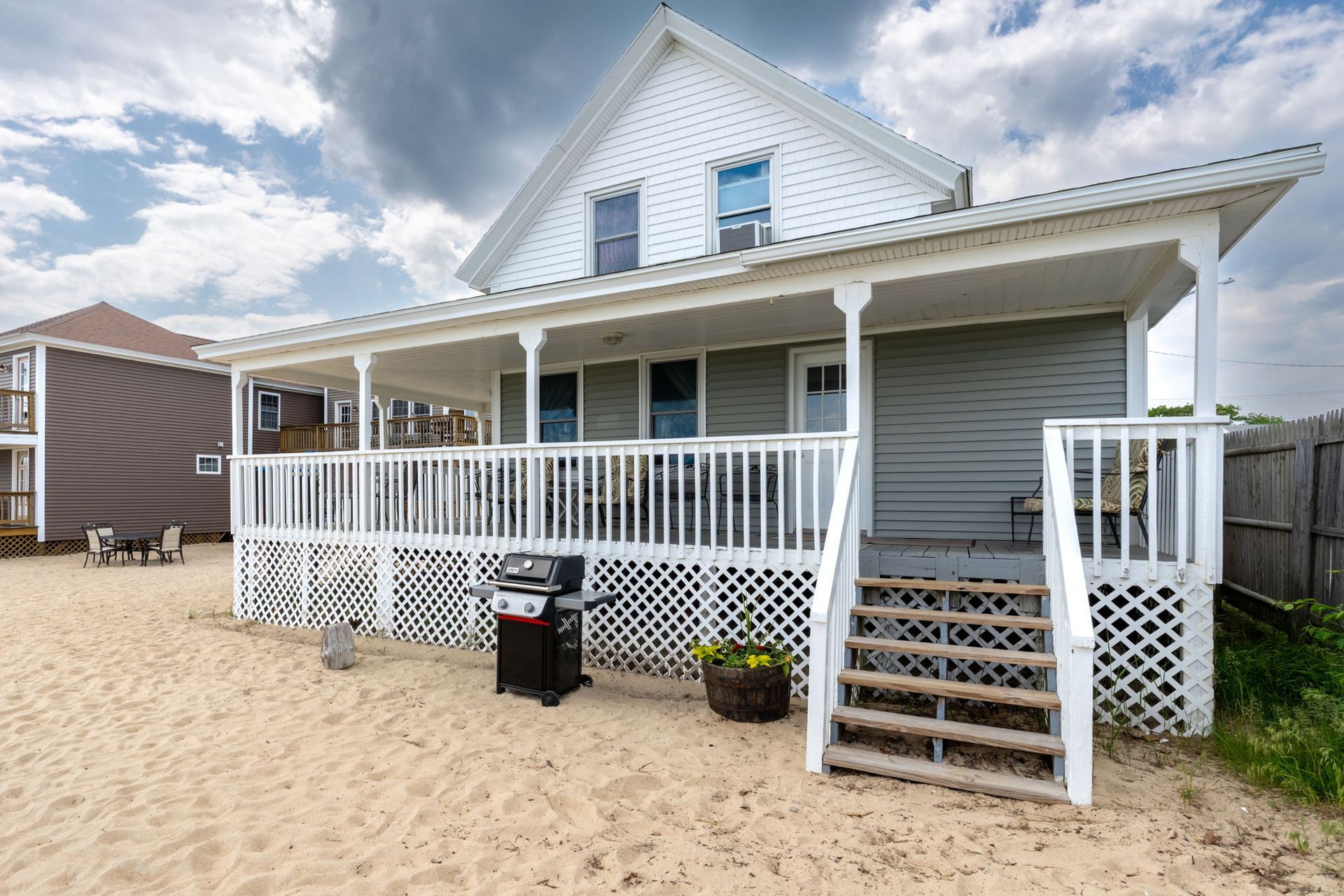 Beachfront house with white porch, gray siding, and a grill on the sand.