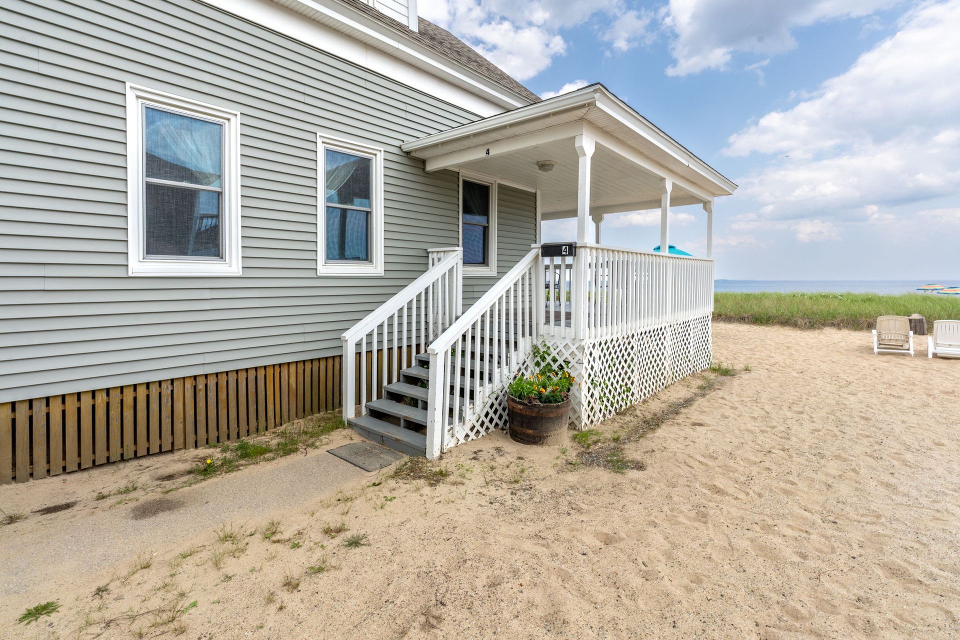Beach house with gray siding and white porch overlooking a sandy beach.
