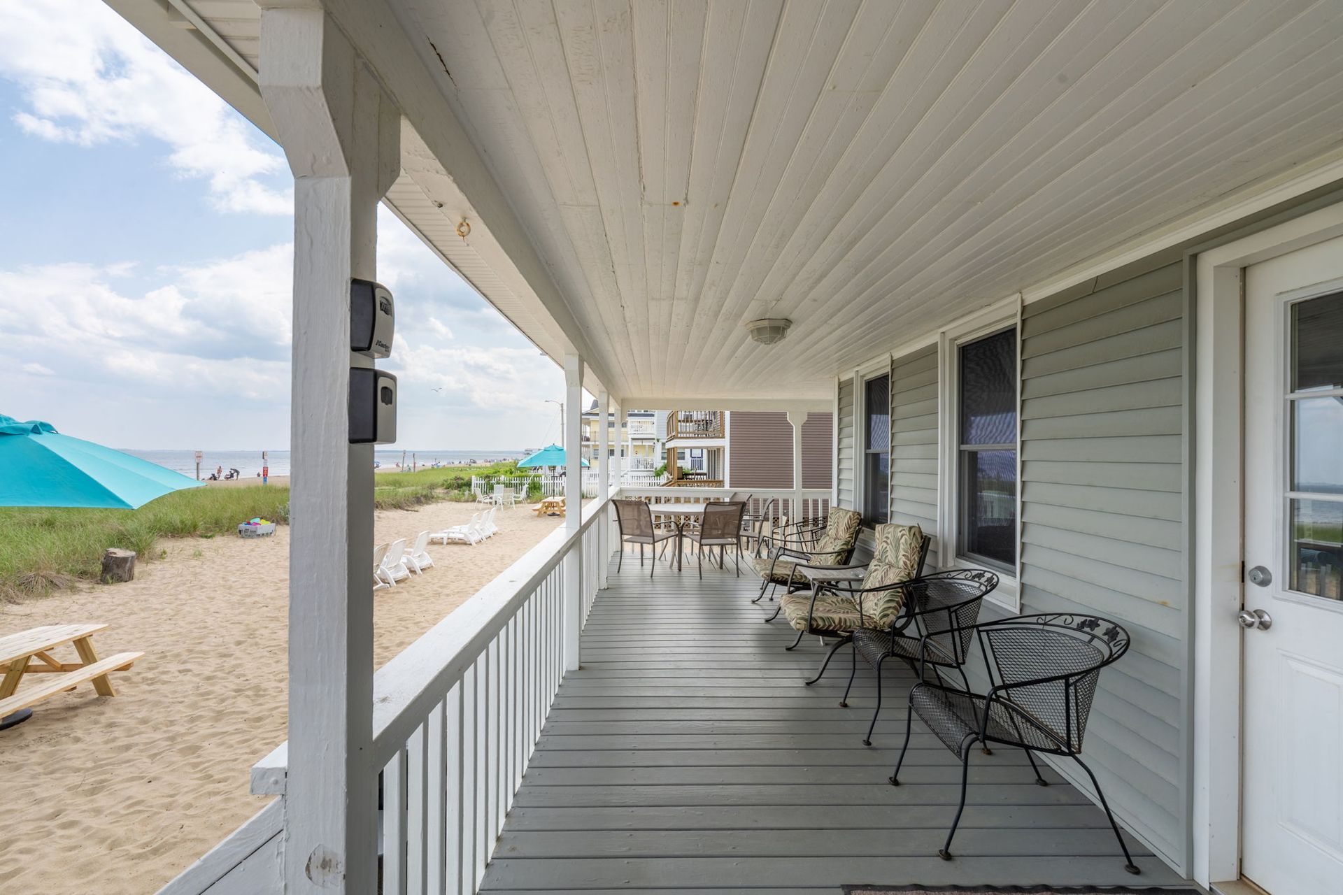 Beachfront porch with chairs and a table, overlooking the sand and ocean.