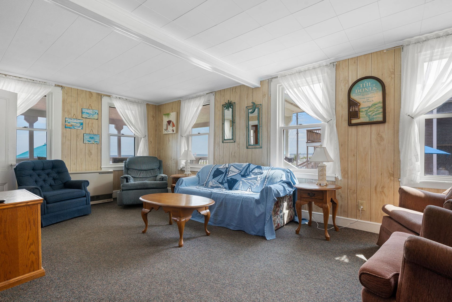 Living room with blue and brown furniture, wood paneling, windows with white curtains.