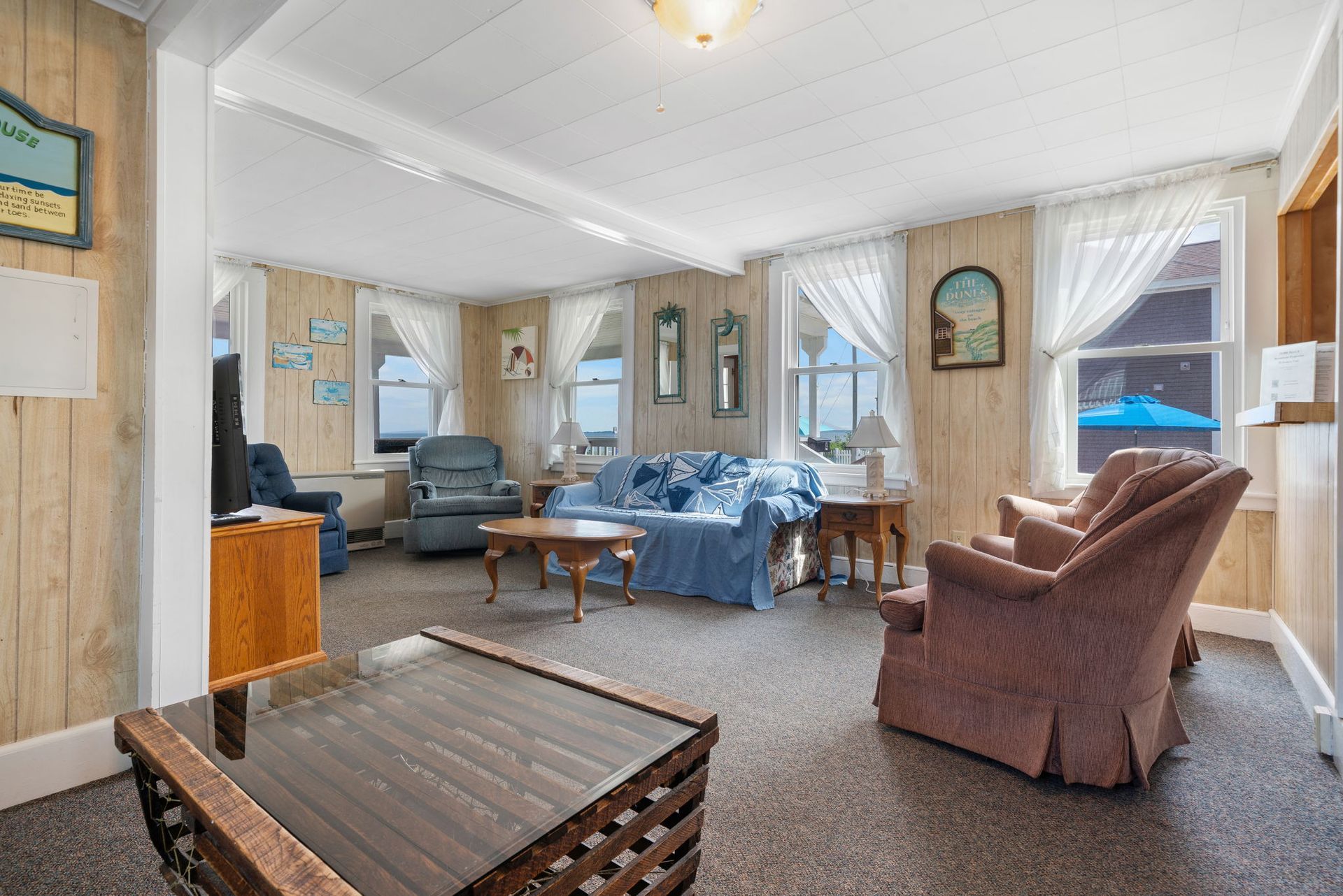 Living room with blue couch, armchairs, and windows with sheer curtains.