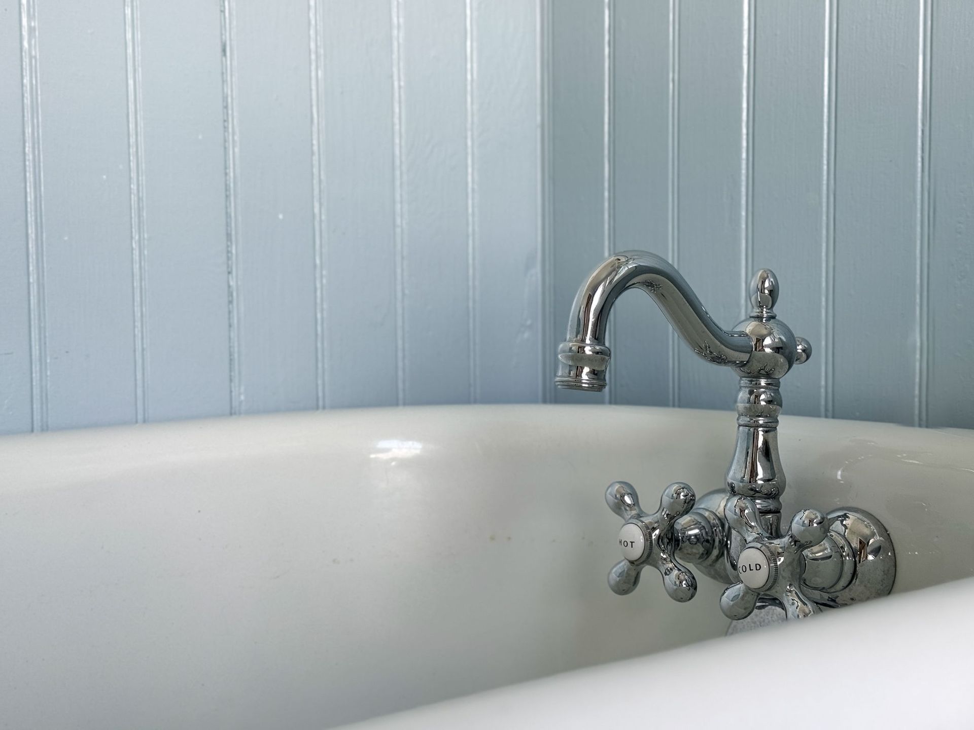 Chrome faucet over a white bathtub against a light blue, paneled wall.