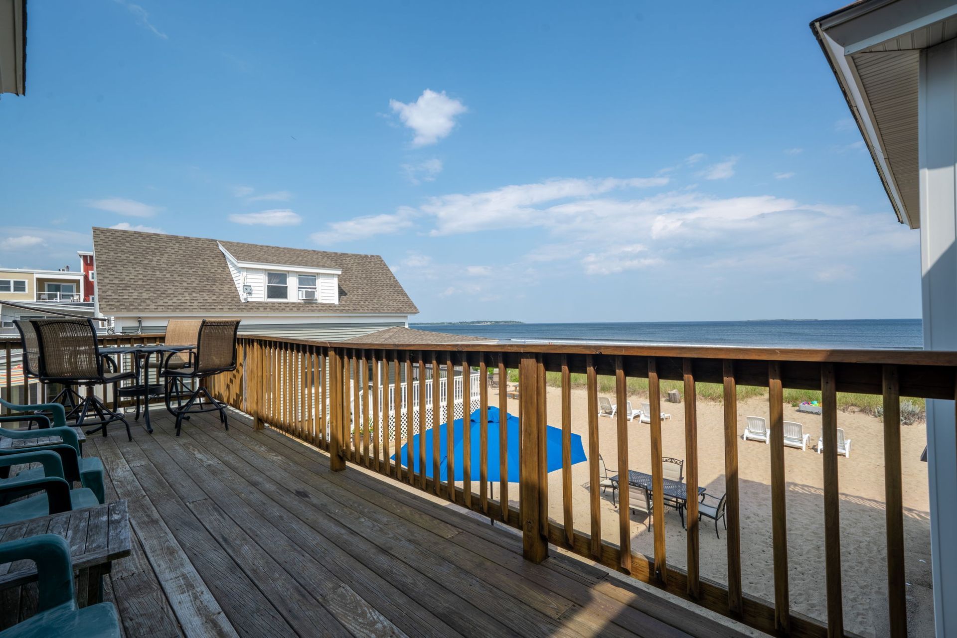 A wooden deck overlooking a beach and ocean with a house and chairs.