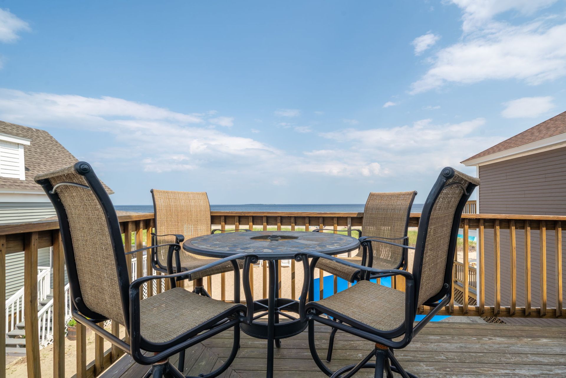 Deck with table and chairs overlooking water, under a blue sky with clouds.
