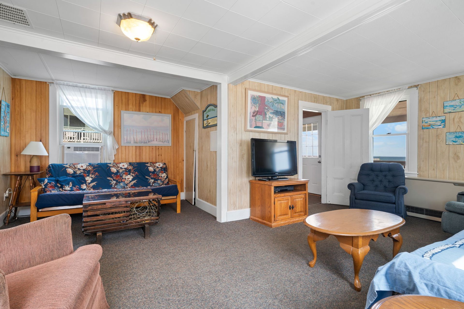 Cozy living room with blue floral futon, wooden furniture, TV, and tan walls.