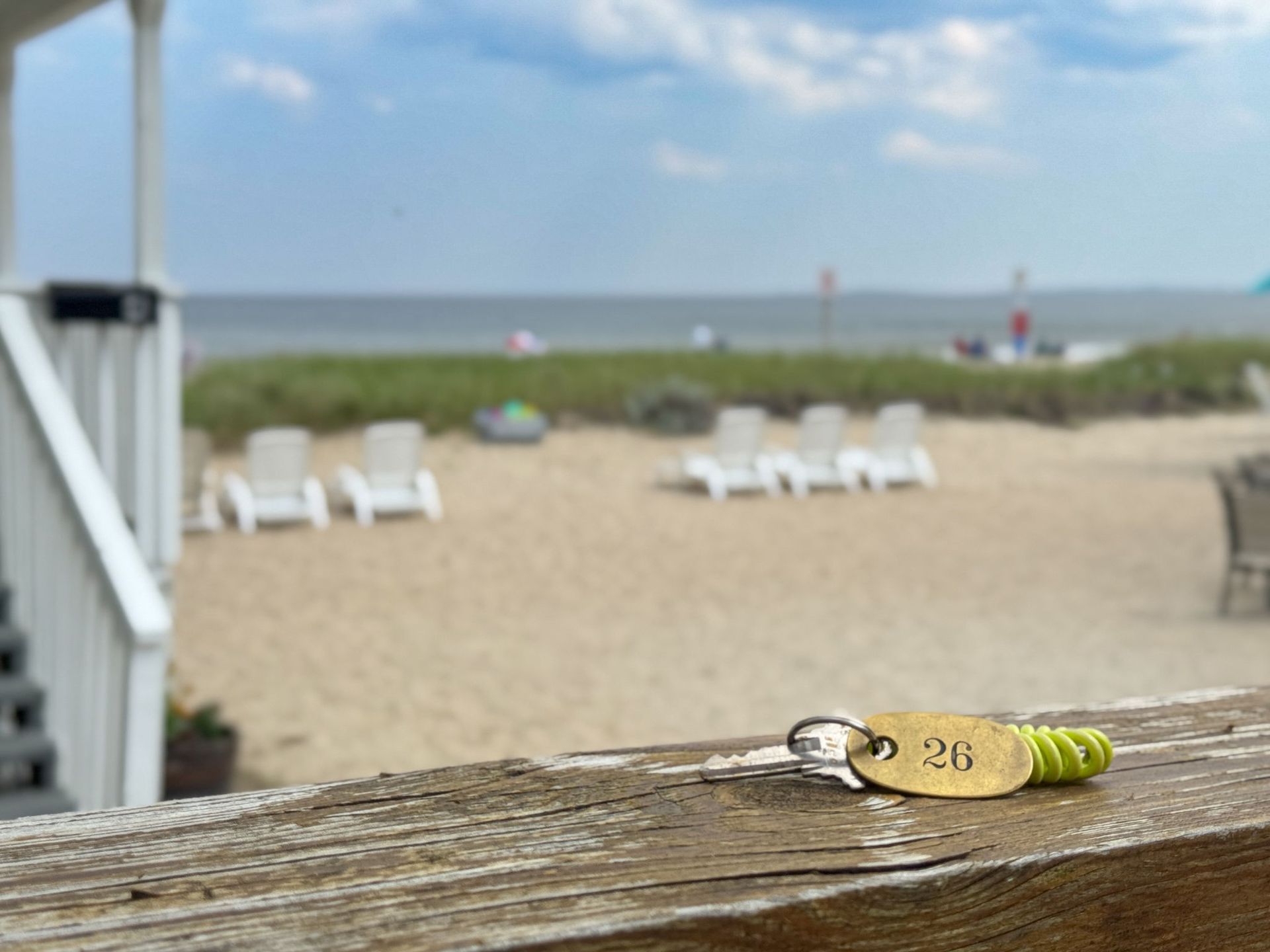 Keys on a wooden railing with a beach view in the background. The key tag has the number 26.