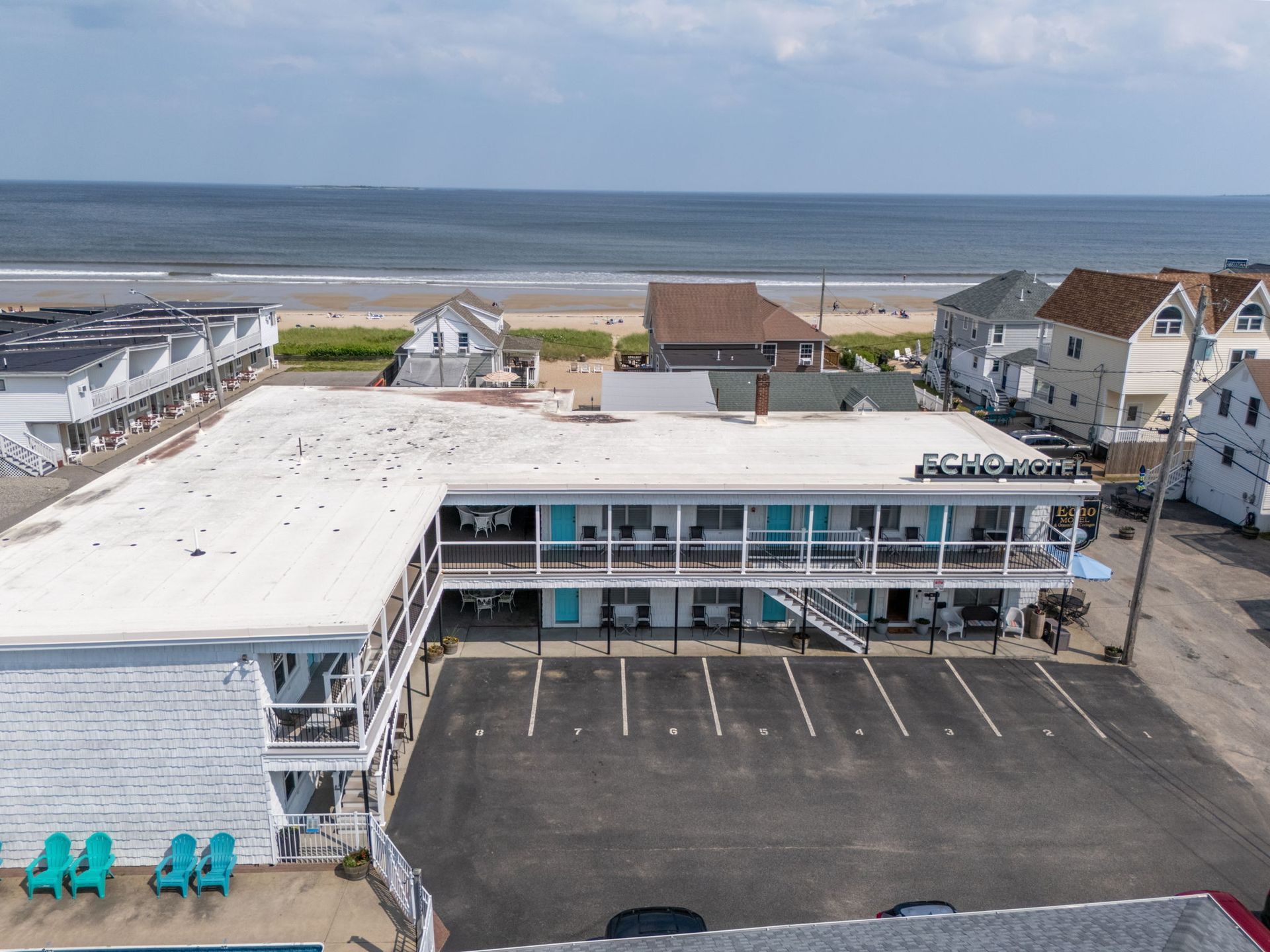 Aerial view of a beachfront motel with parking lot, ocean, and blue sky.