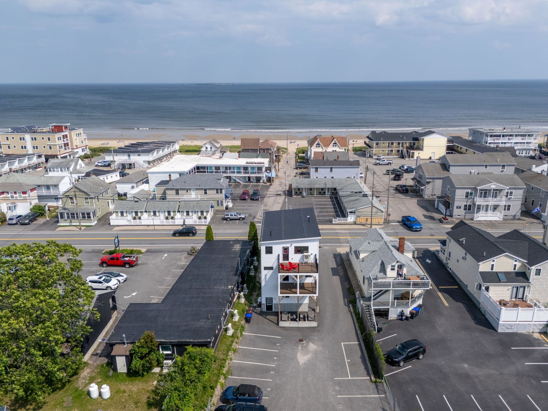 Aerial view of a beach town with buildings, a street, and ocean in the background on a sunny day.