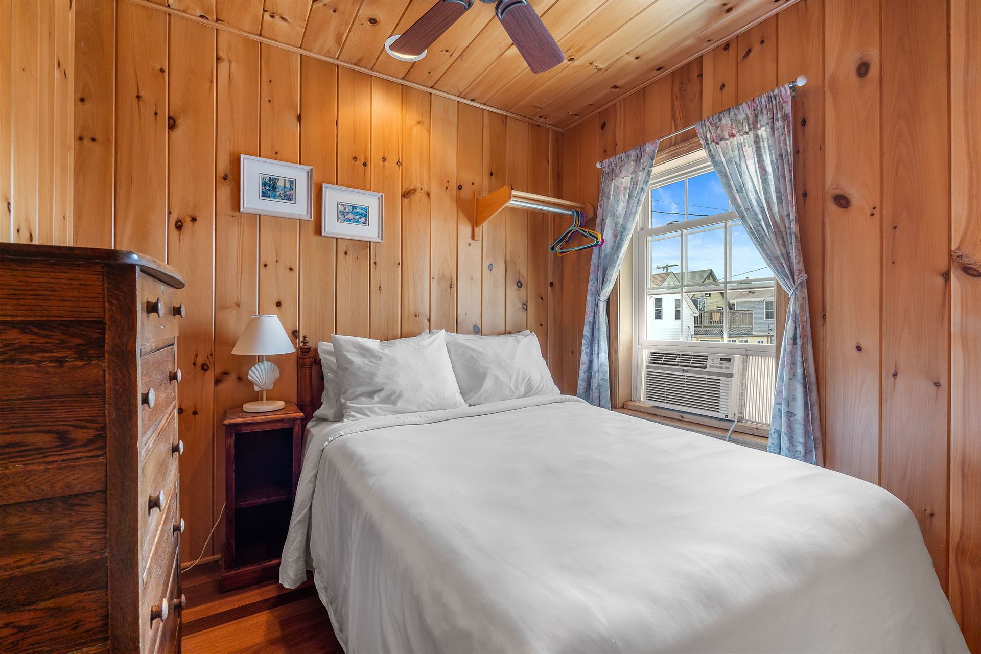Small bedroom with wood paneling, bed, and window with blue curtains.