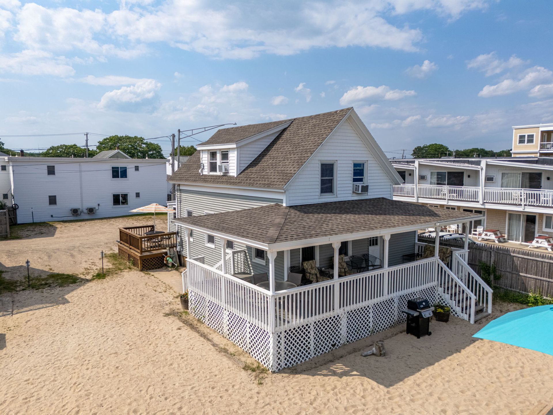 White beach house with porch and sandy yard under blue sky.