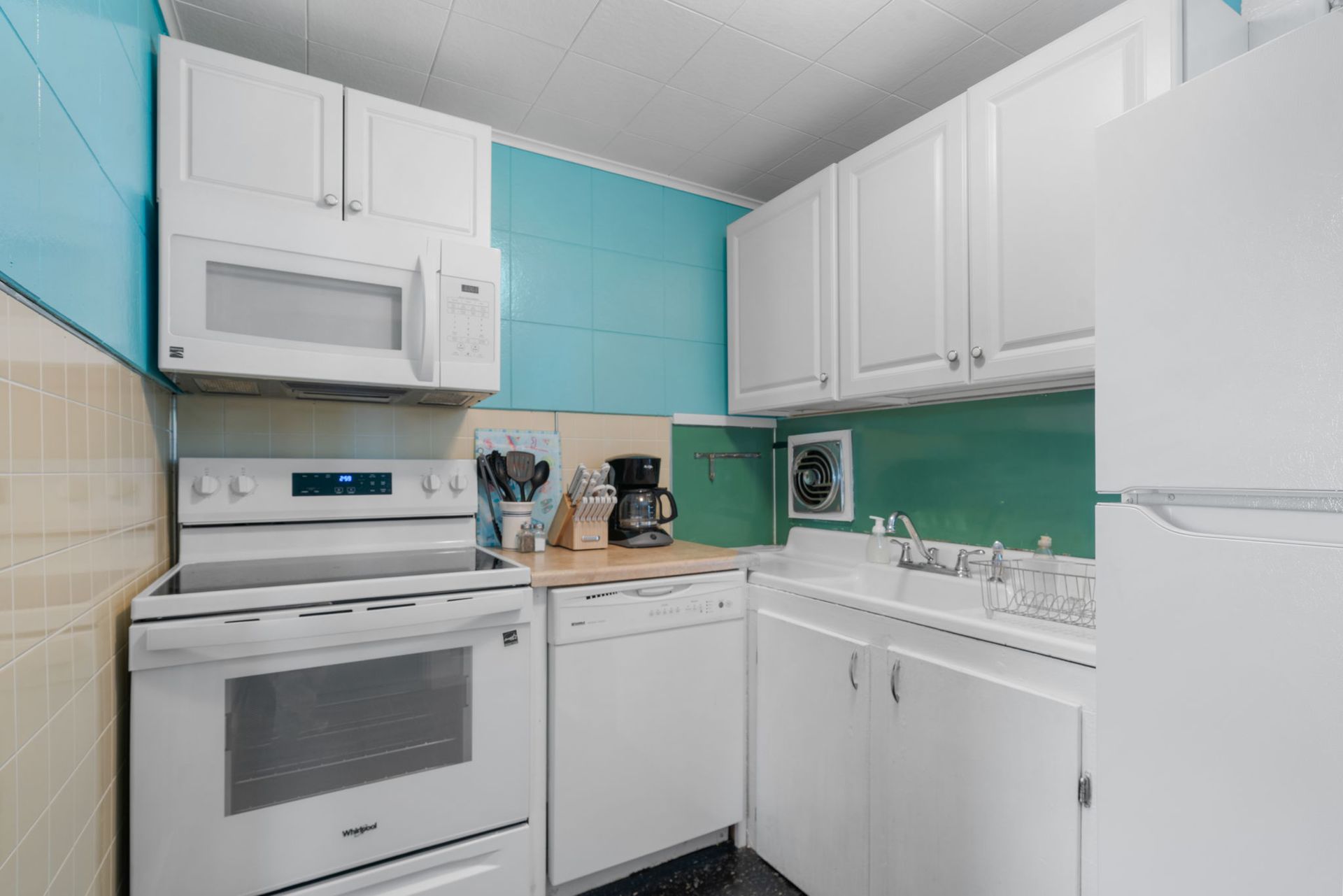 Small kitchen with white appliances, cabinets, and turquoise walls.