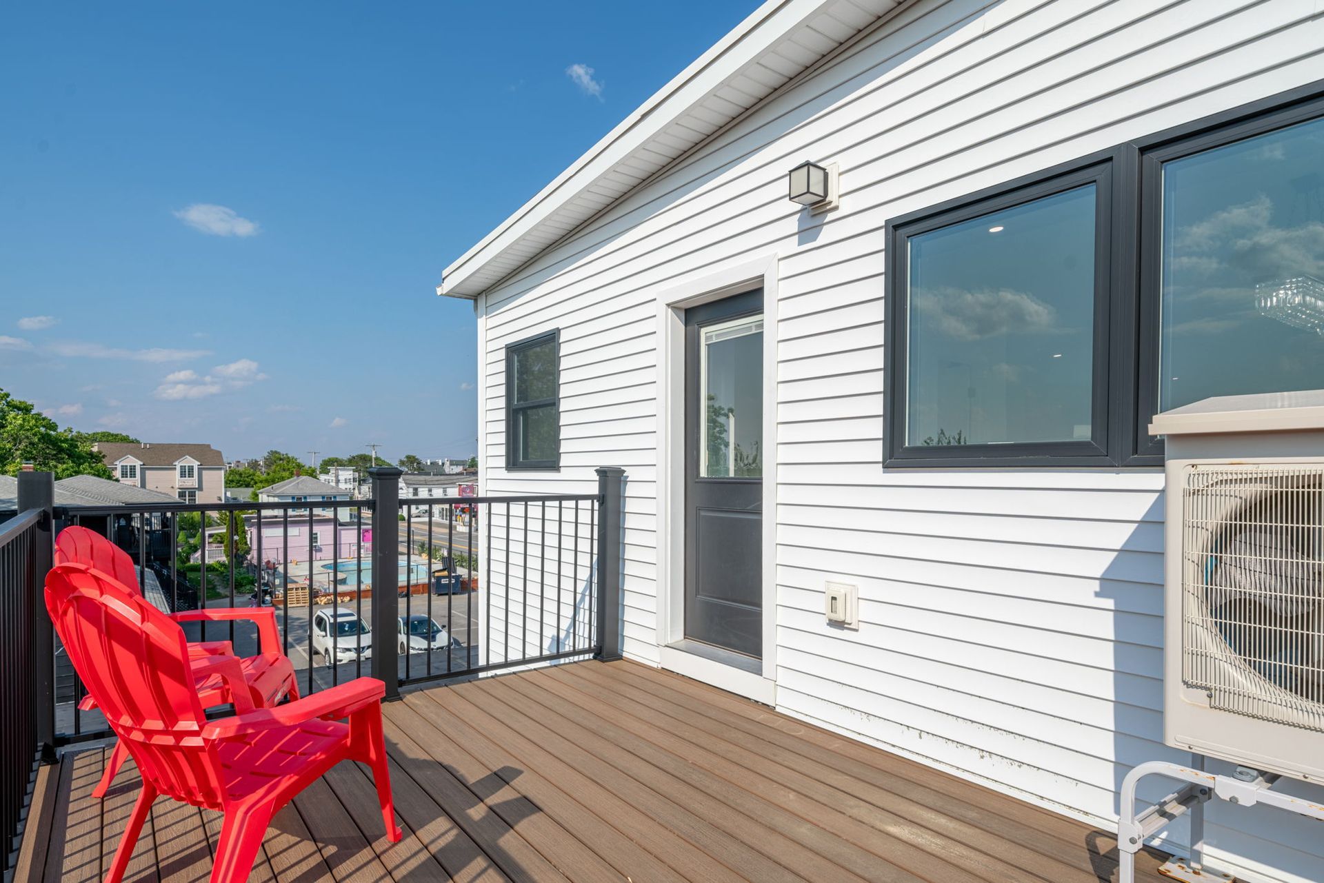 Rooftop deck with red chair, black railing, and white building under a blue sky.