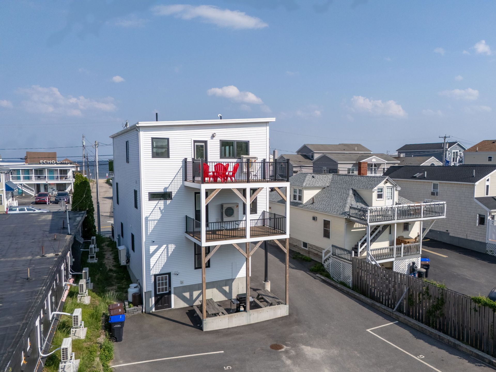 White multi-story building with decks; clothes drying on top balcony. Sunny day in a coastal town.