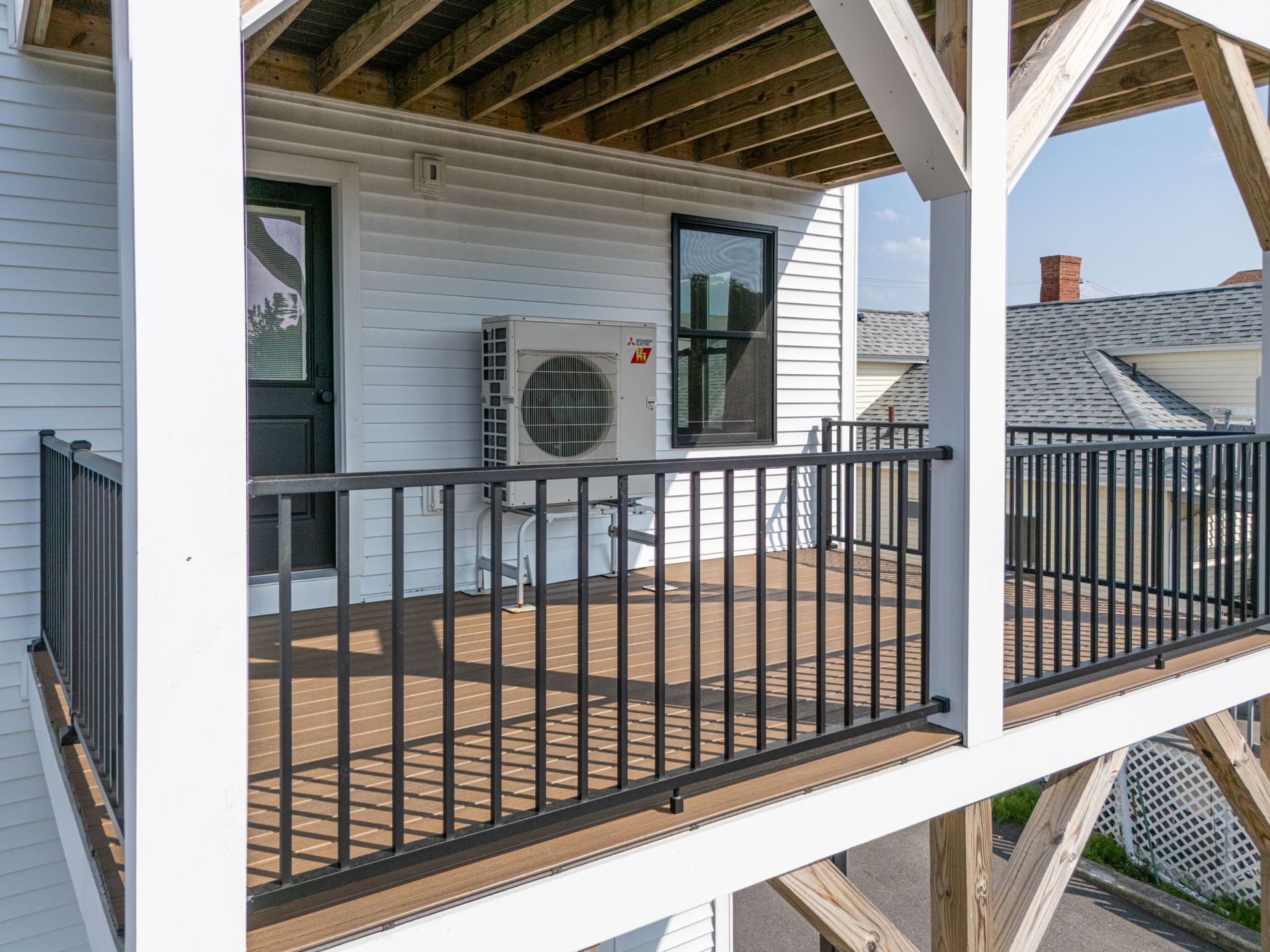 Balcony with black railing, white siding, an AC unit, and a dark door.