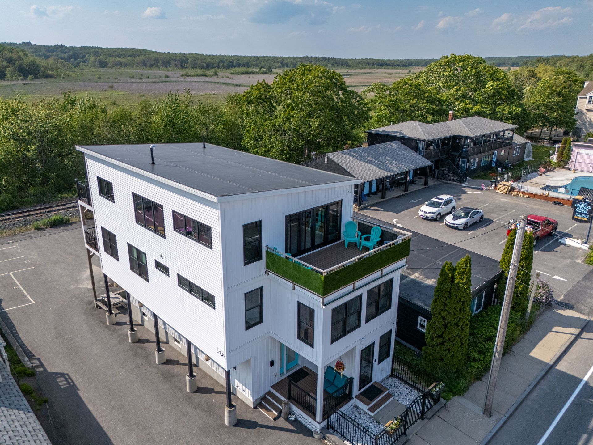 Modern white multi-story building with small green rooftop, blue chairs, set in front of a marsh.