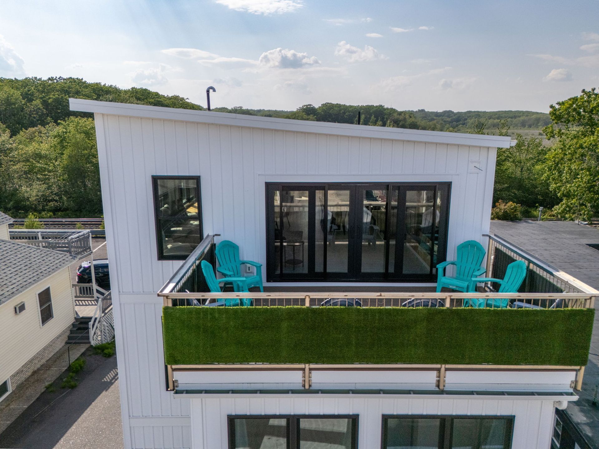 White building with rooftop deck and blue chairs, overlooking green trees and cloudy sky.