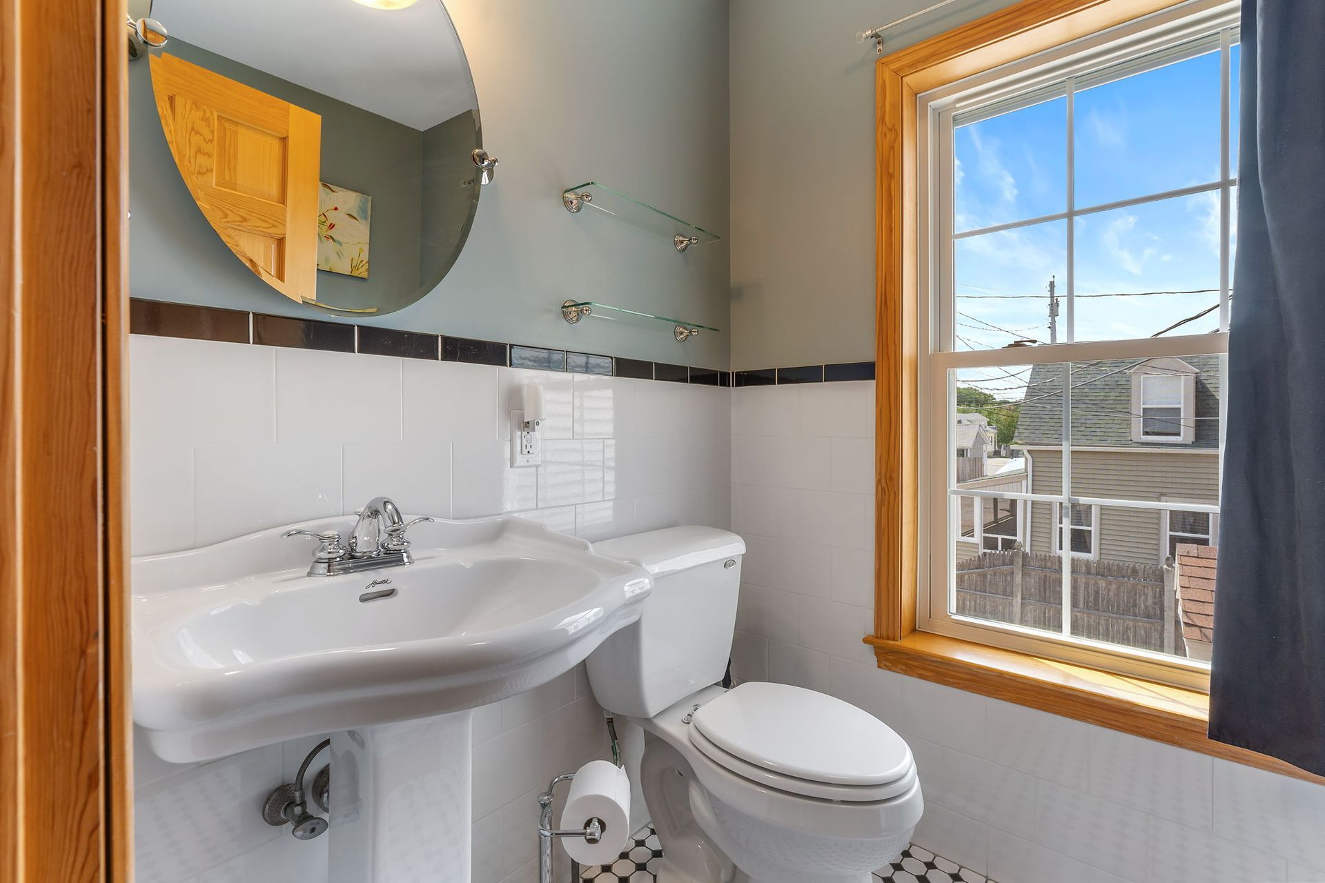 Bathroom with white fixtures, black and white tile floor, and window with a view of buildings.