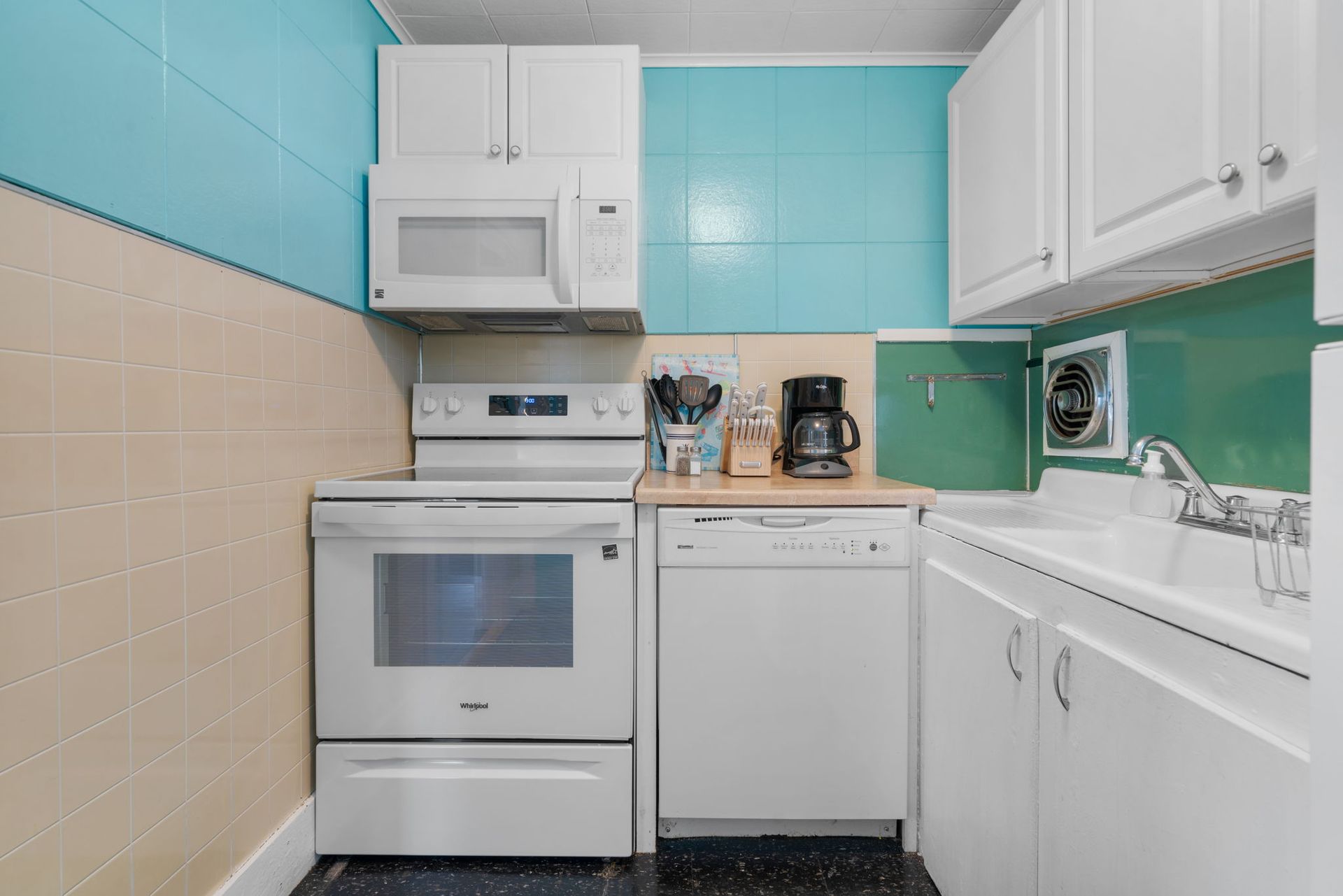 A small, white kitchen with teal and beige walls. Appliances include a microwave, oven, and dishwasher.