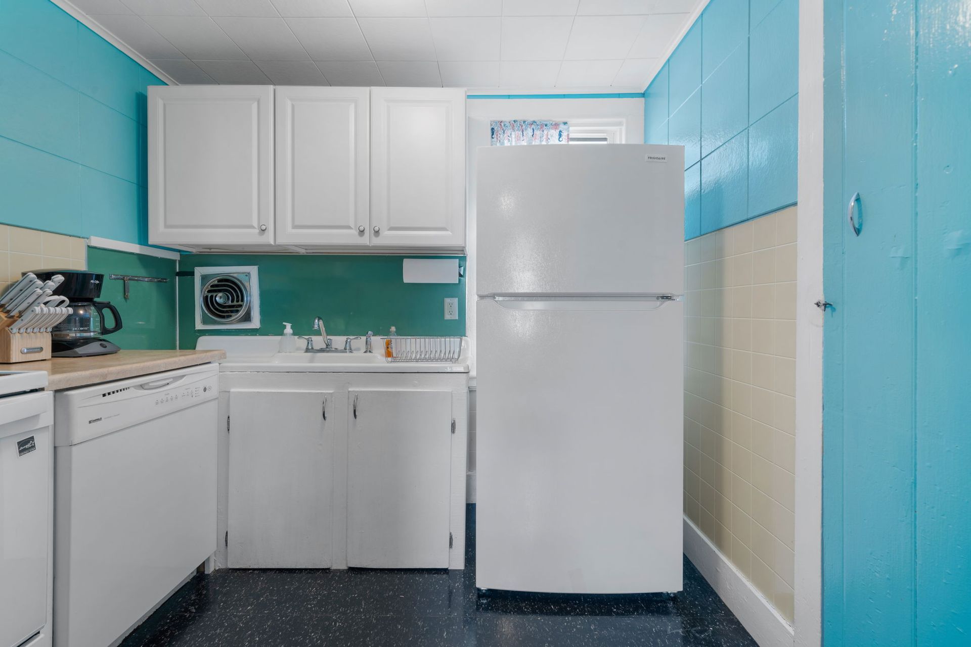 White kitchen with blue and yellow walls, white cabinets and appliances, dark floor.