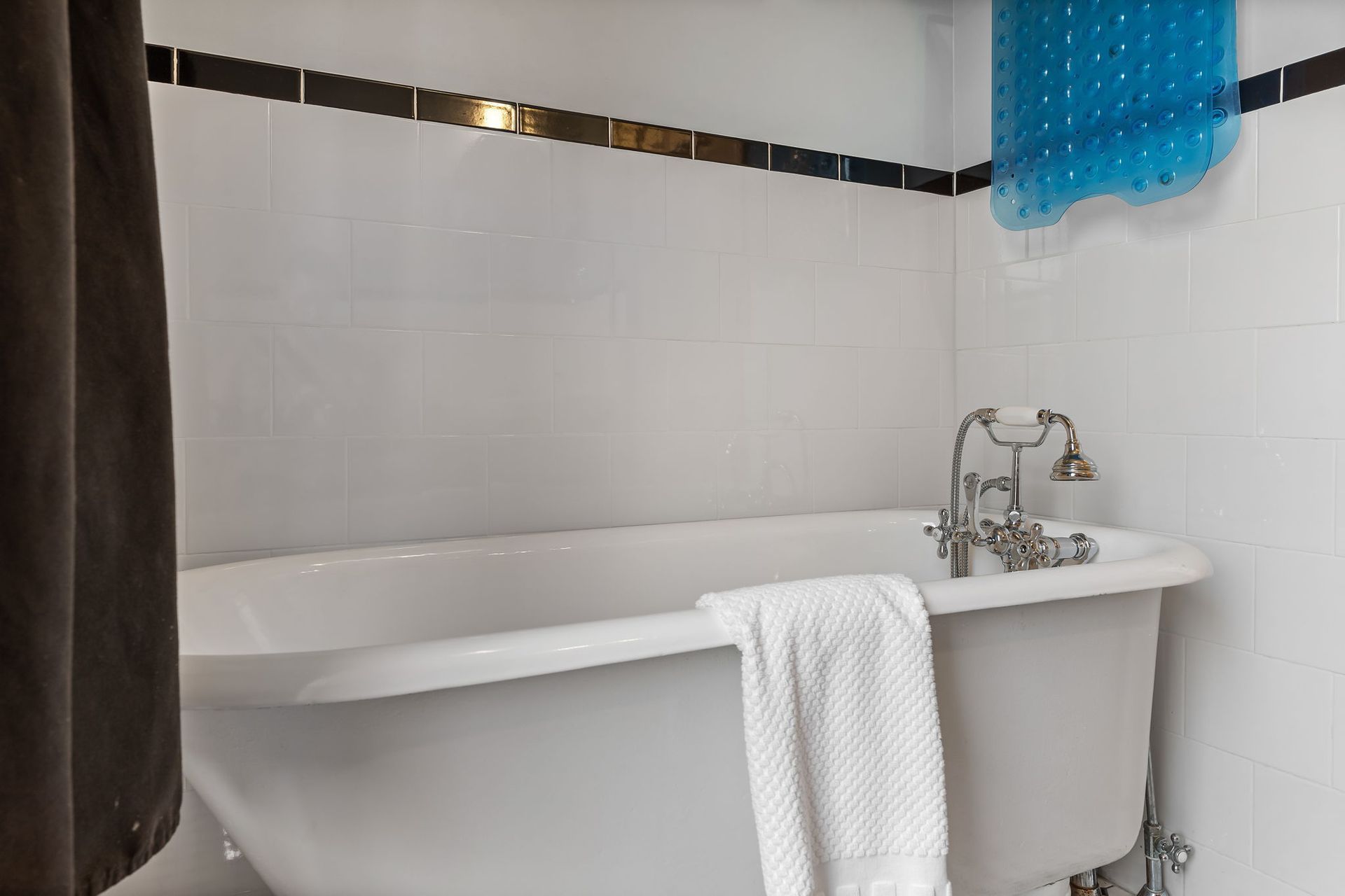 White bathtub with chrome fixtures in a tiled bathroom; white towel, blue shower curtain.