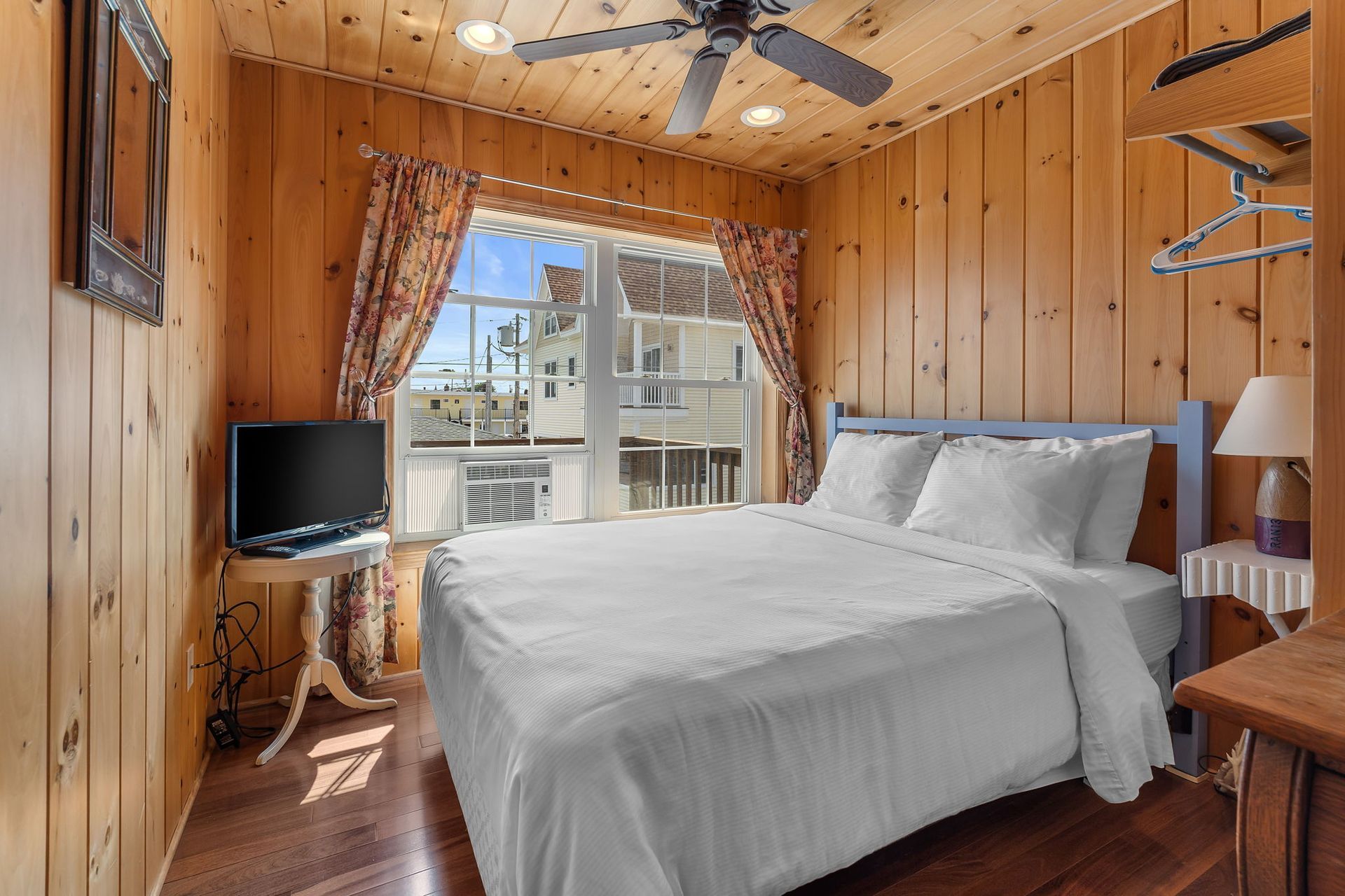 Bedroom with a double bed, wood-paneled walls, a window with curtains, and a ceiling fan.
