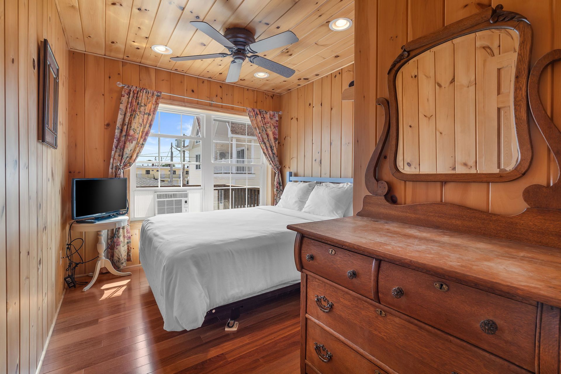 Bedroom with wood paneling, bed, dresser, window with view, and a ceiling fan.