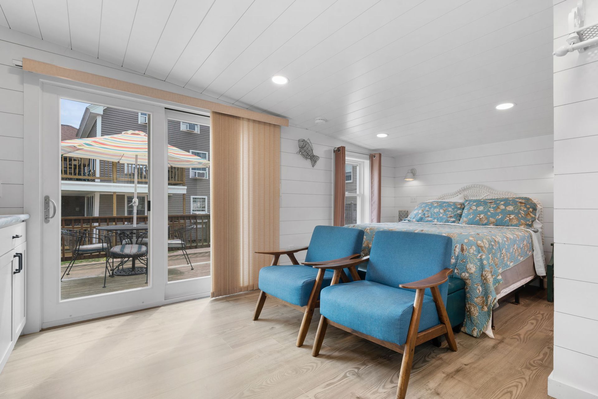Bedroom with blue chairs, a bed with floral bedding, and a sliding door to a patio.