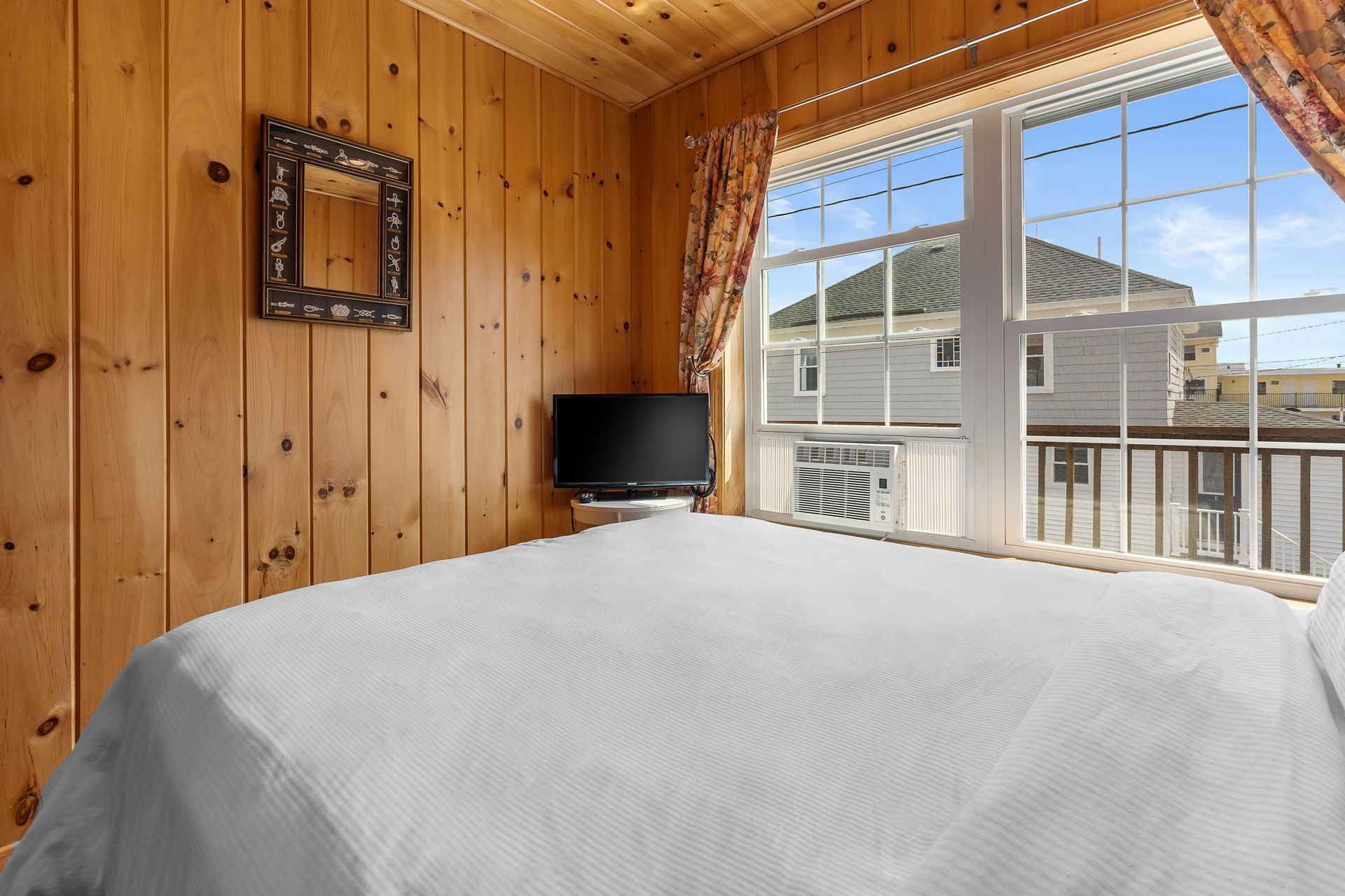 Bedroom with wood-paneled walls, a window with a view, a bed, and a small TV.
