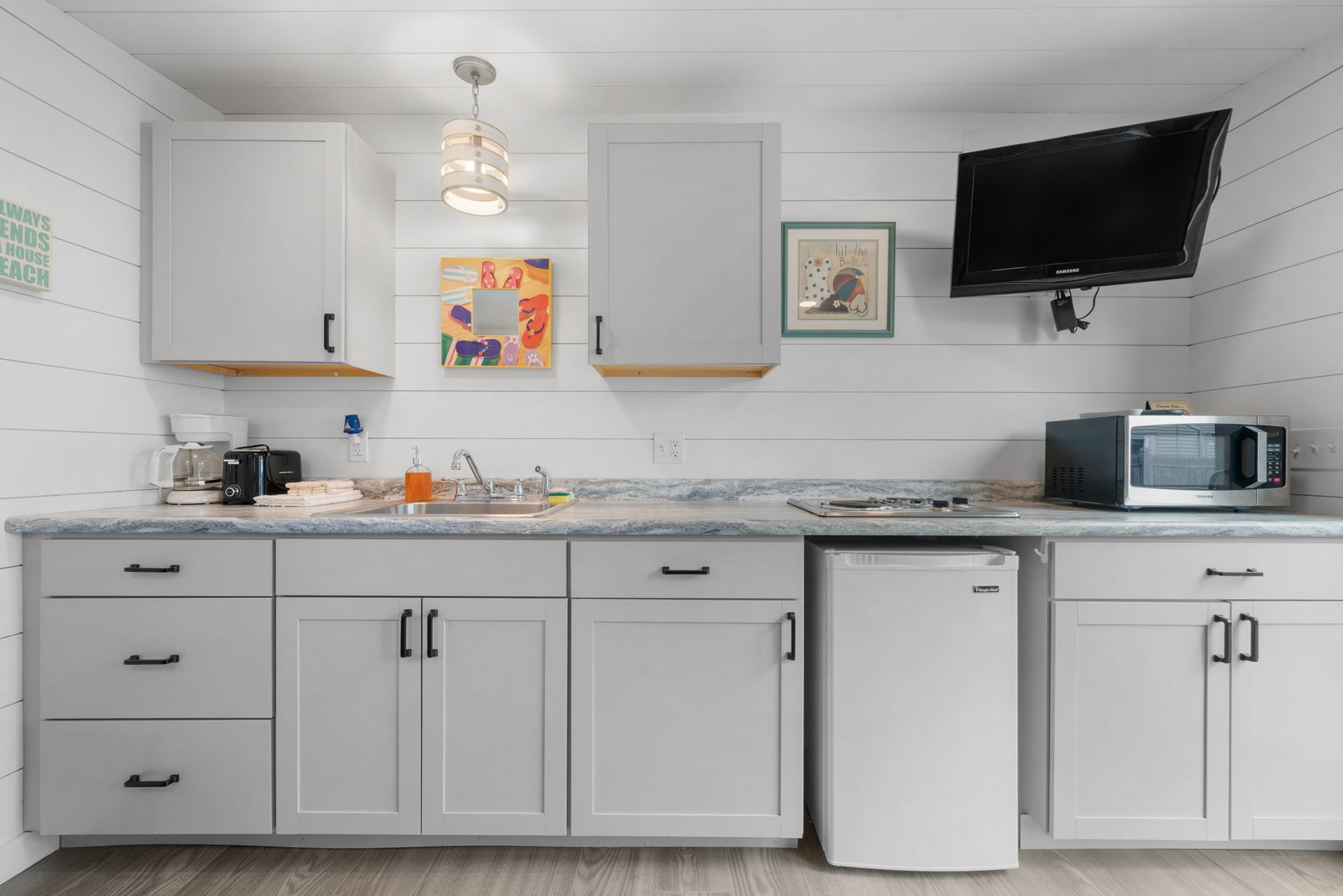 Small kitchen with gray cabinets, white appliances, and a mounted TV.