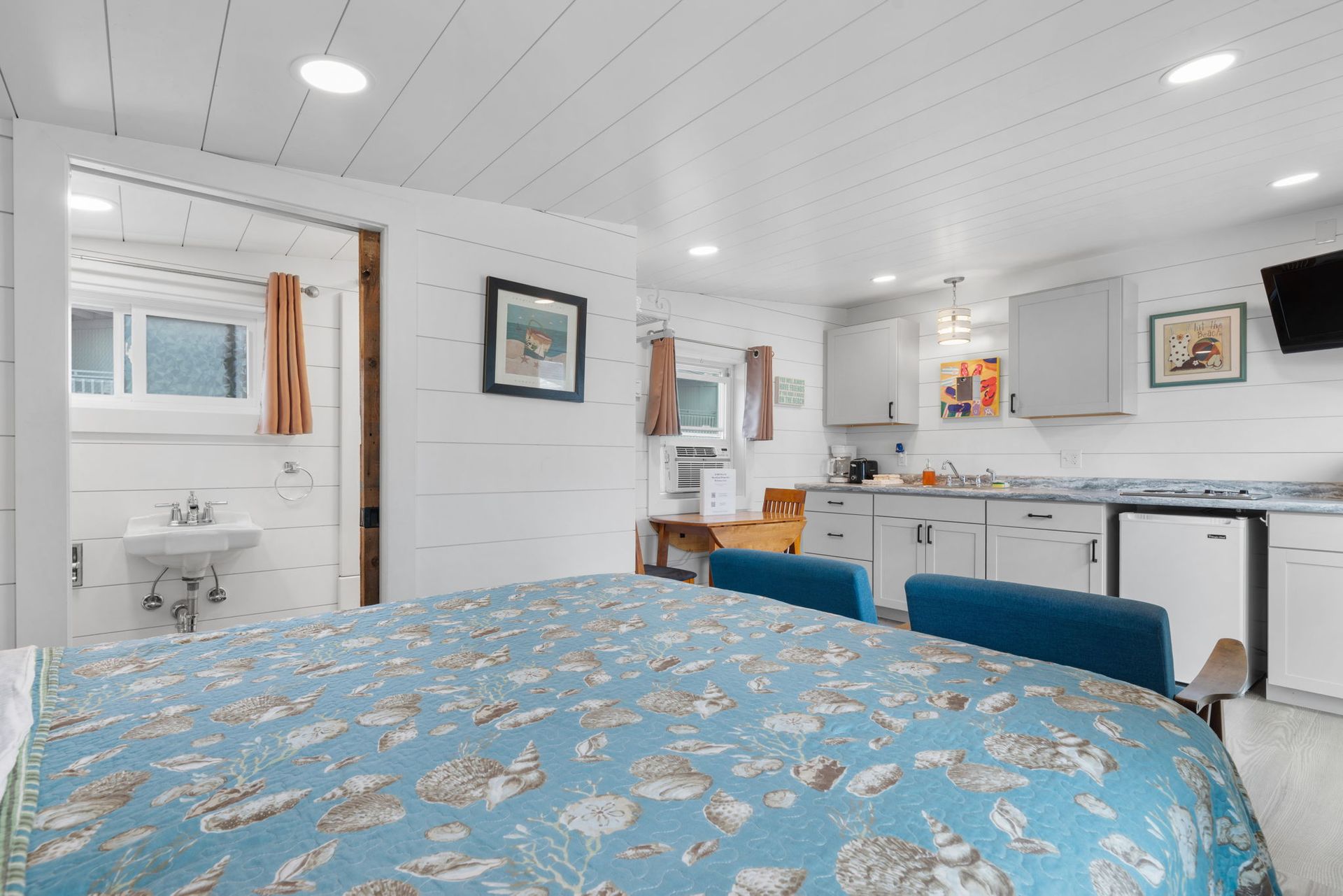 Small, bright studio apartment with bed, kitchenette, and bathroom. White walls, blue bedspread.