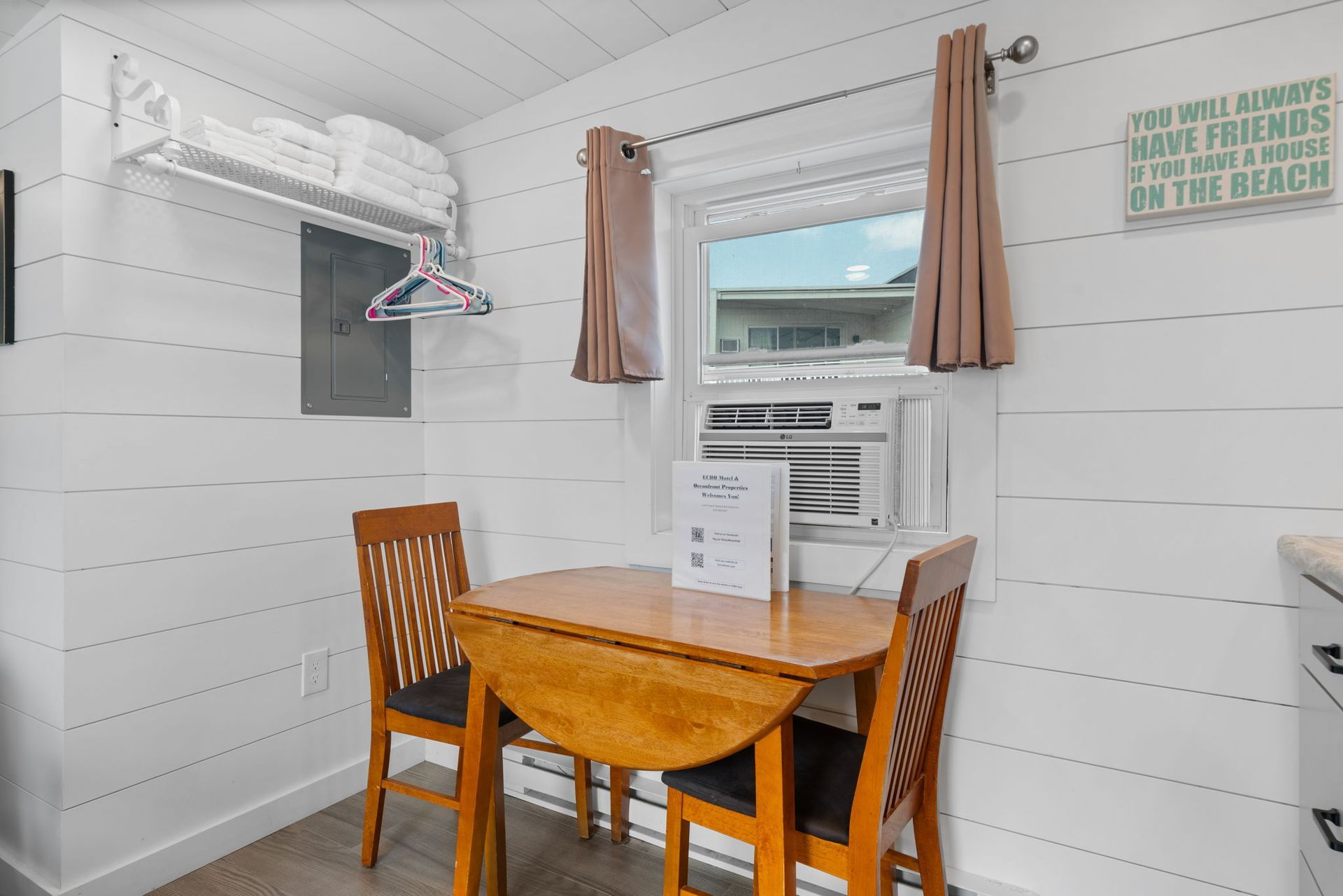 A small room with a table and chairs, a window with a/c, and a sign on the table.