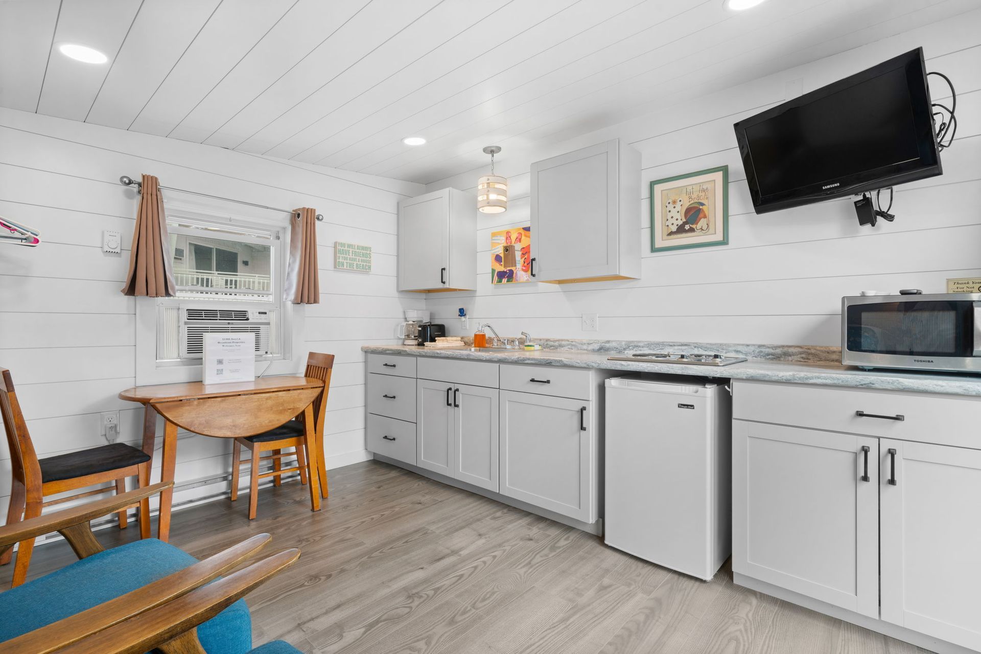 Small kitchen with white cabinets, countertop, and appliances, with a TV and dining table.