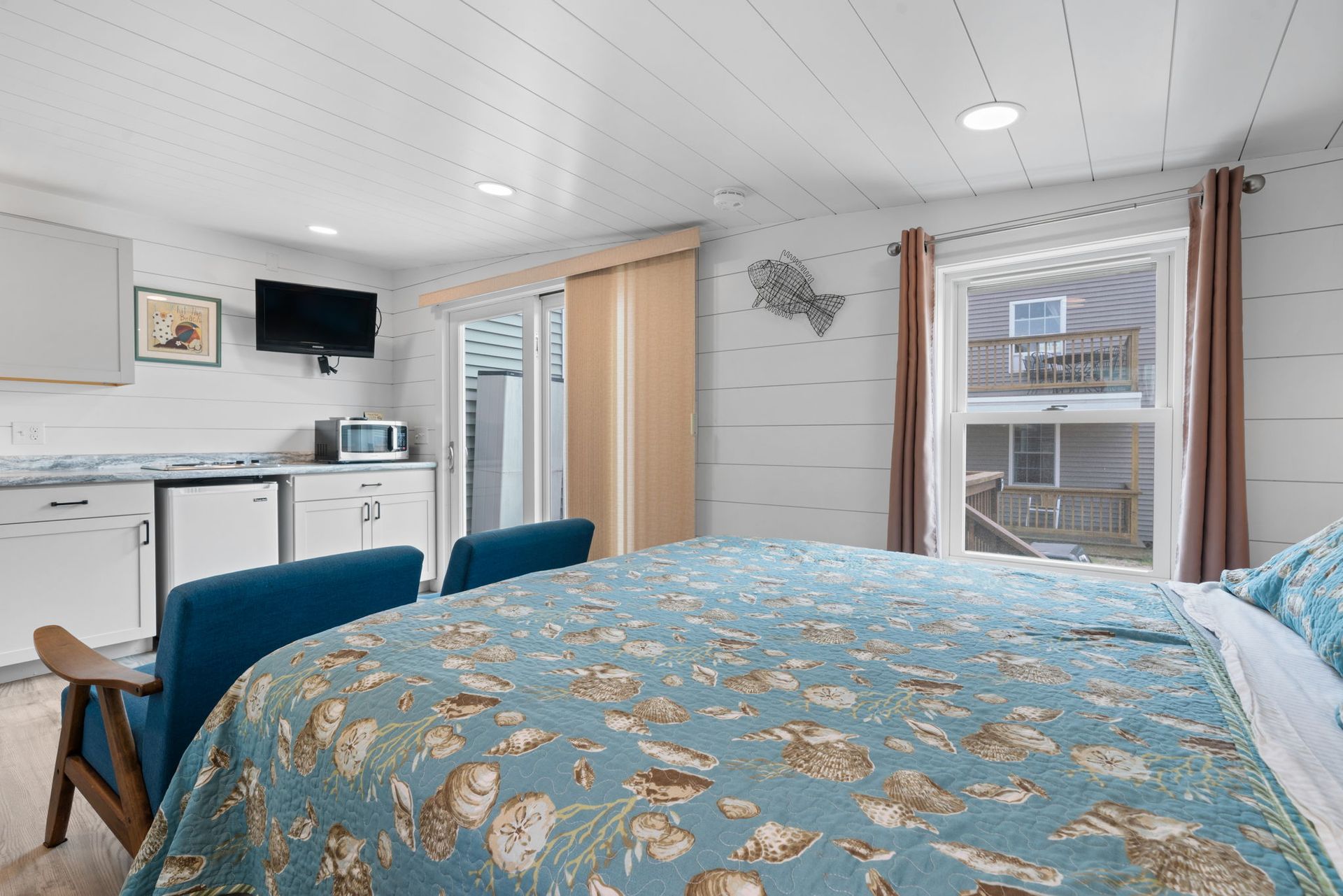 Small studio bedroom with a queen bed, kitchenette, and sliding door to a balcony.
