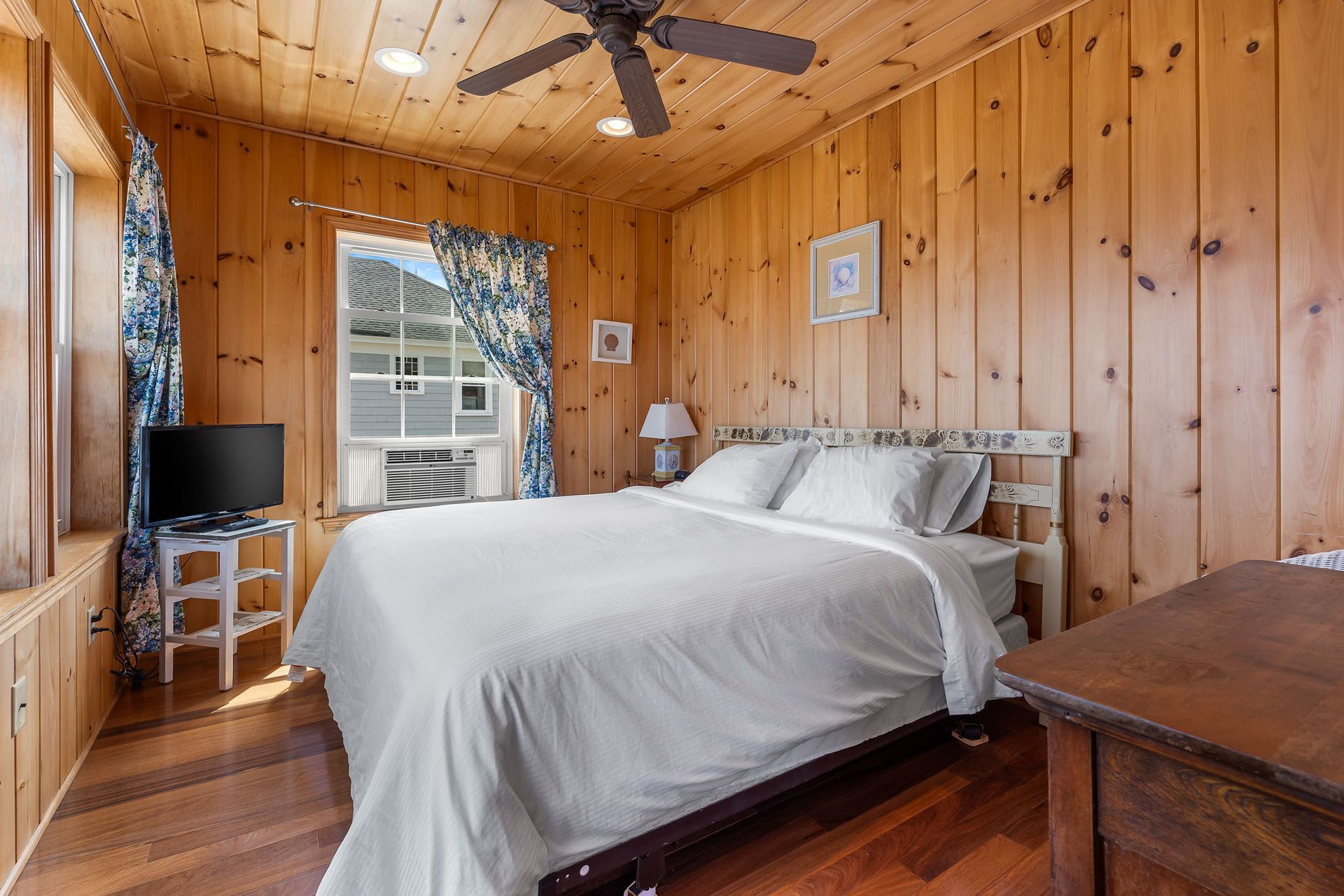 Bedroom with wood-paneled walls, queen bed, TV, and floral curtains.