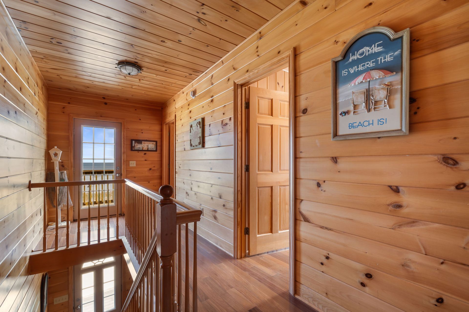 Hallway with wood paneling, stairs, open door, and beach-themed wall decor.