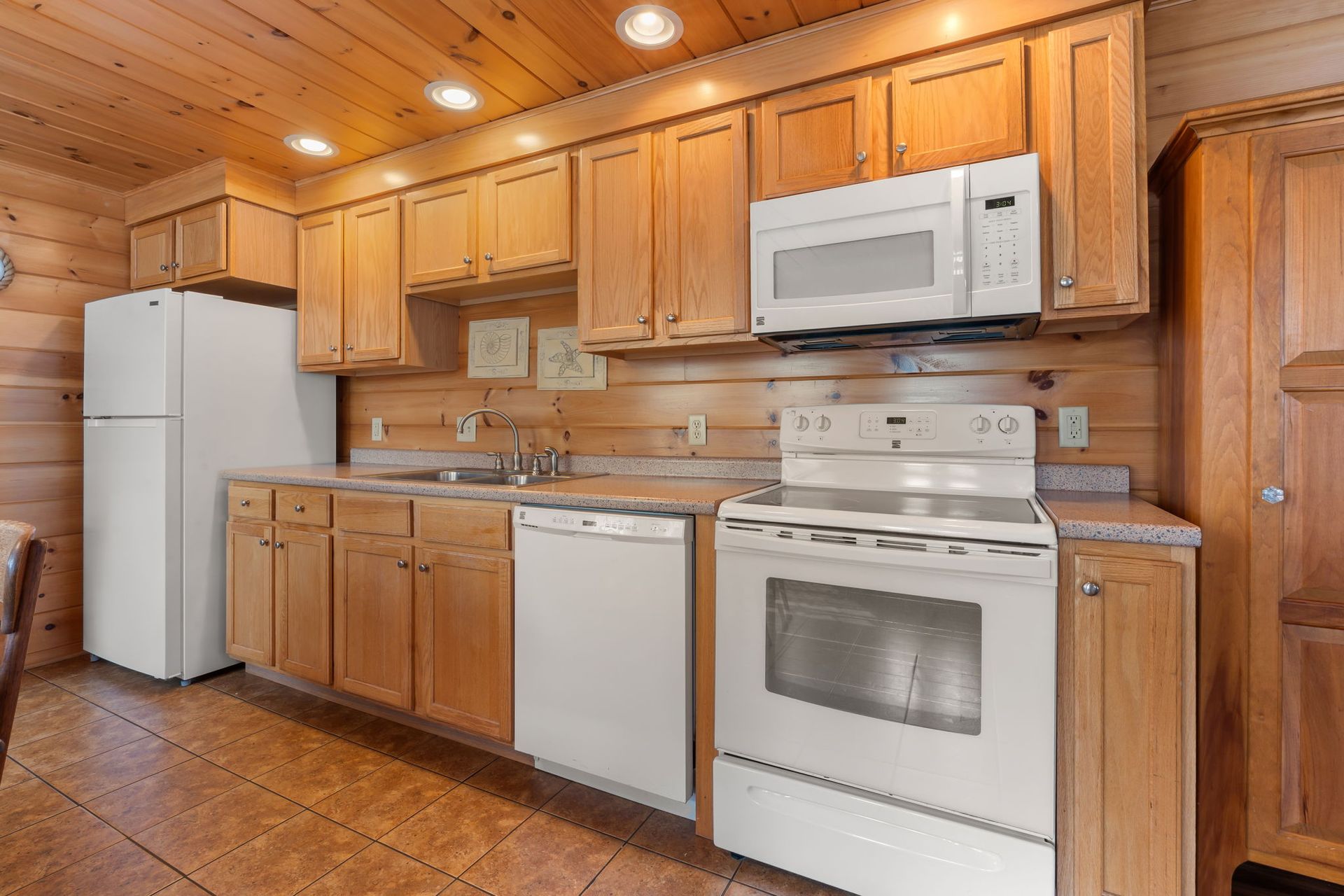 Kitchen with light wood cabinets, white appliances, and brown tiled floor.