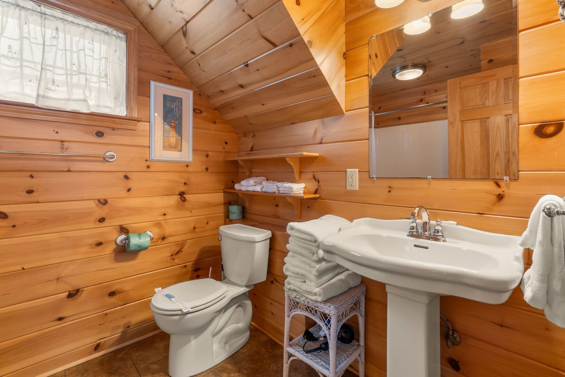 Bathroom with wood paneling, pedestal sink, toilet, and stacked towels.